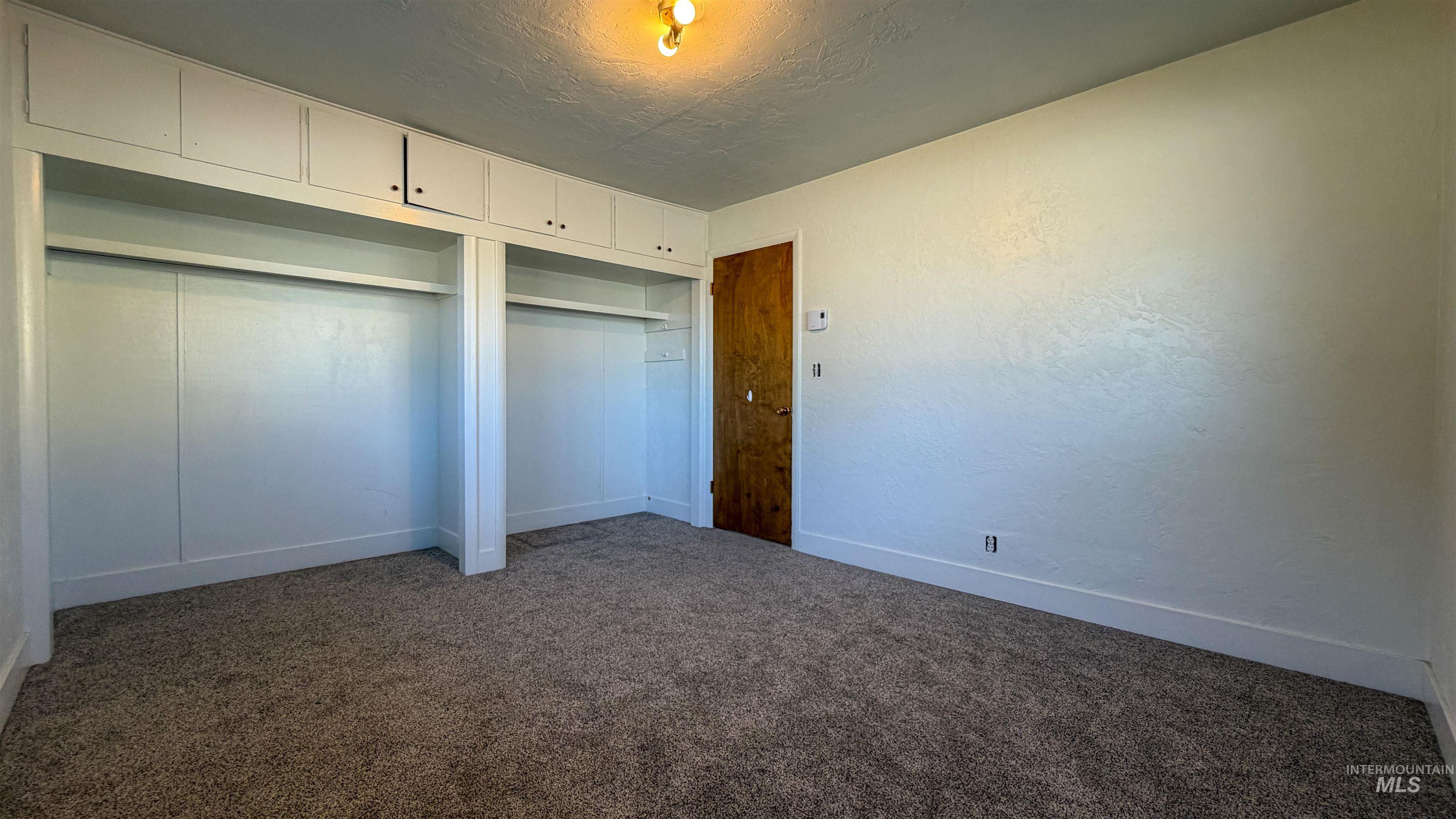 Unfurnished bedroom featuring a textured ceiling, dark carpet, two closets, and a textured wall