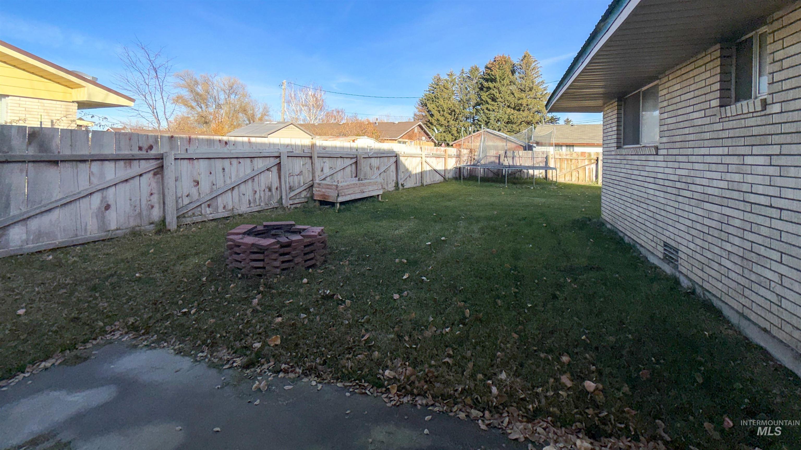 Fenced backyard with a trampoline, a fire pit, and a gate