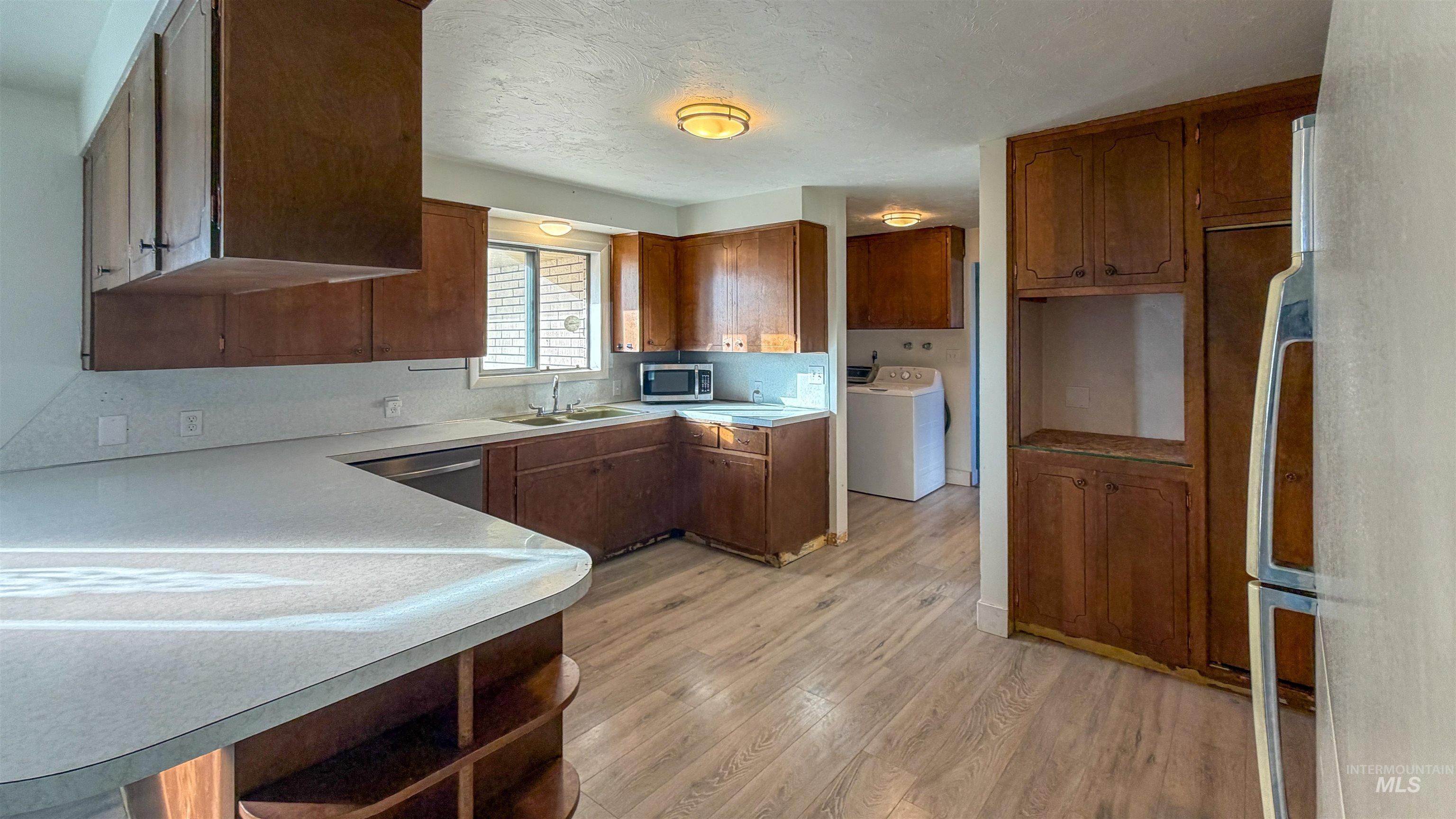 Kitchen featuring light wood-type flooring, brown cabinetry, light countertops, open shelves, and a textured ceiling