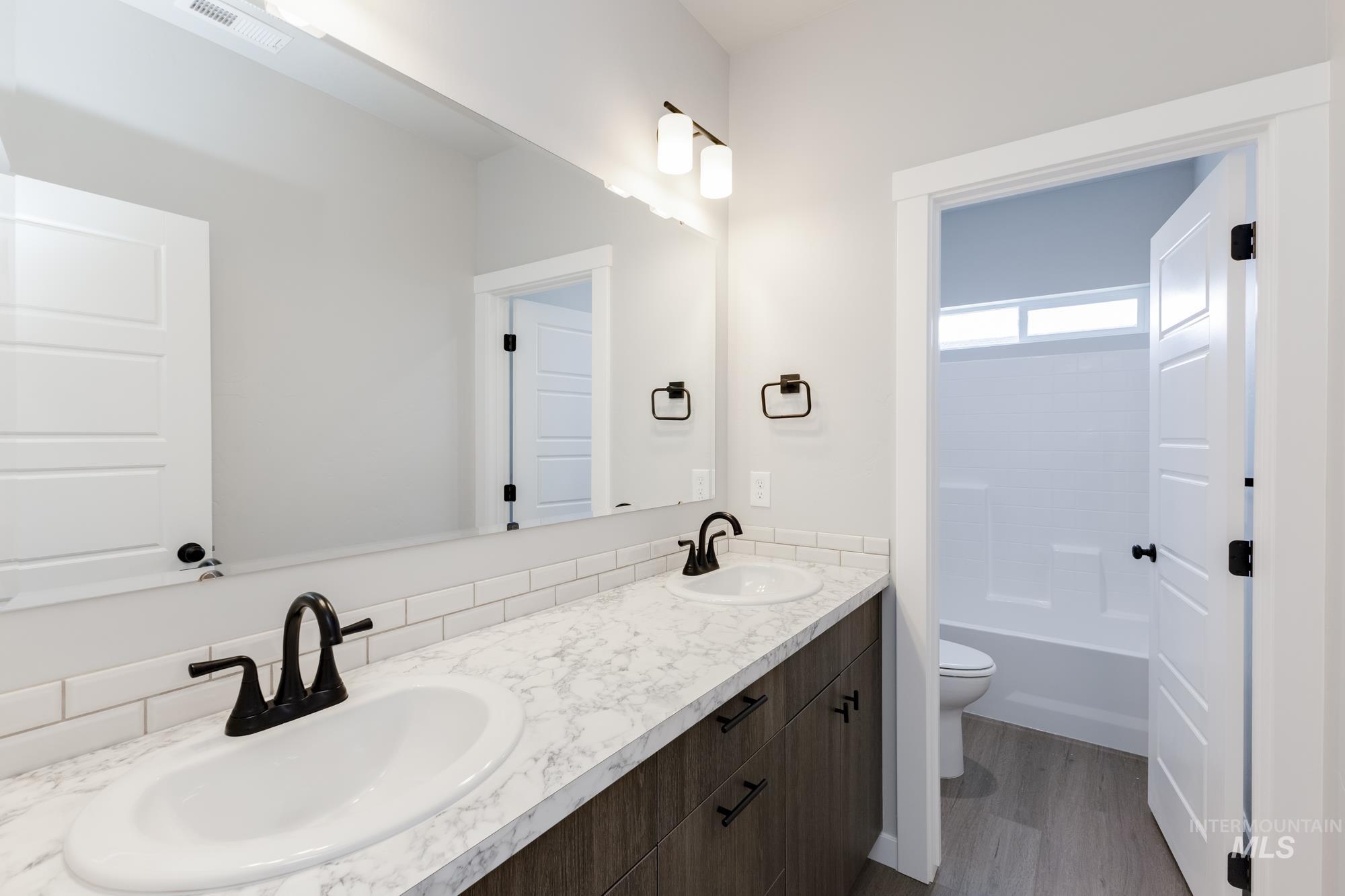 Full bath with double vanity, dark wood-type flooring, and tub / shower combination