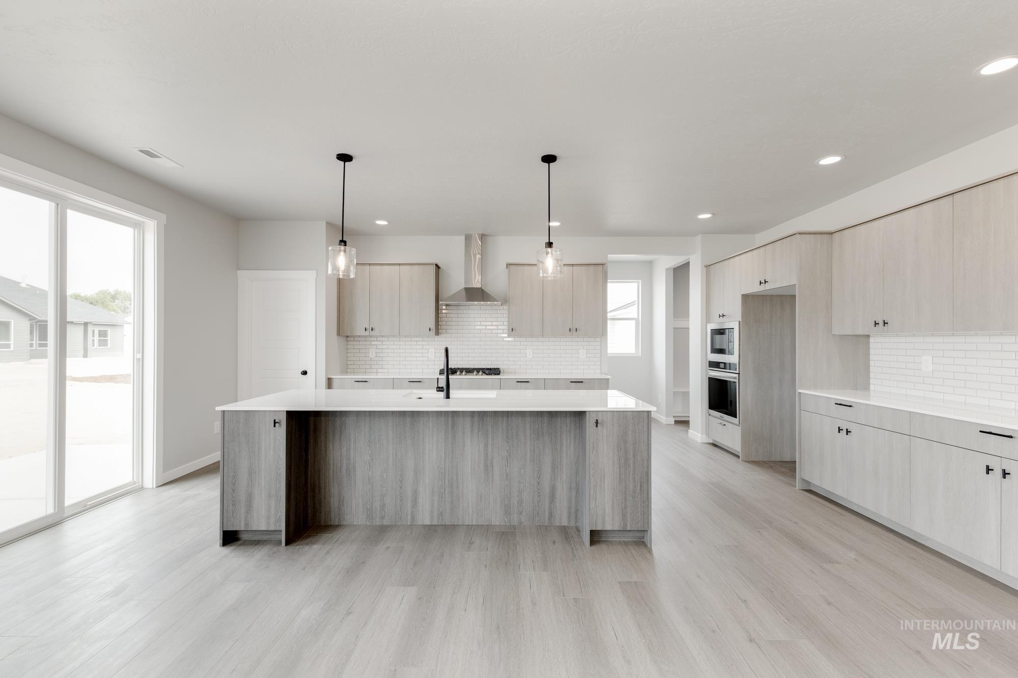 Kitchen featuring an island with sink, tasteful backsplash, light stone counters, light wood-style flooring, and recessed lighting