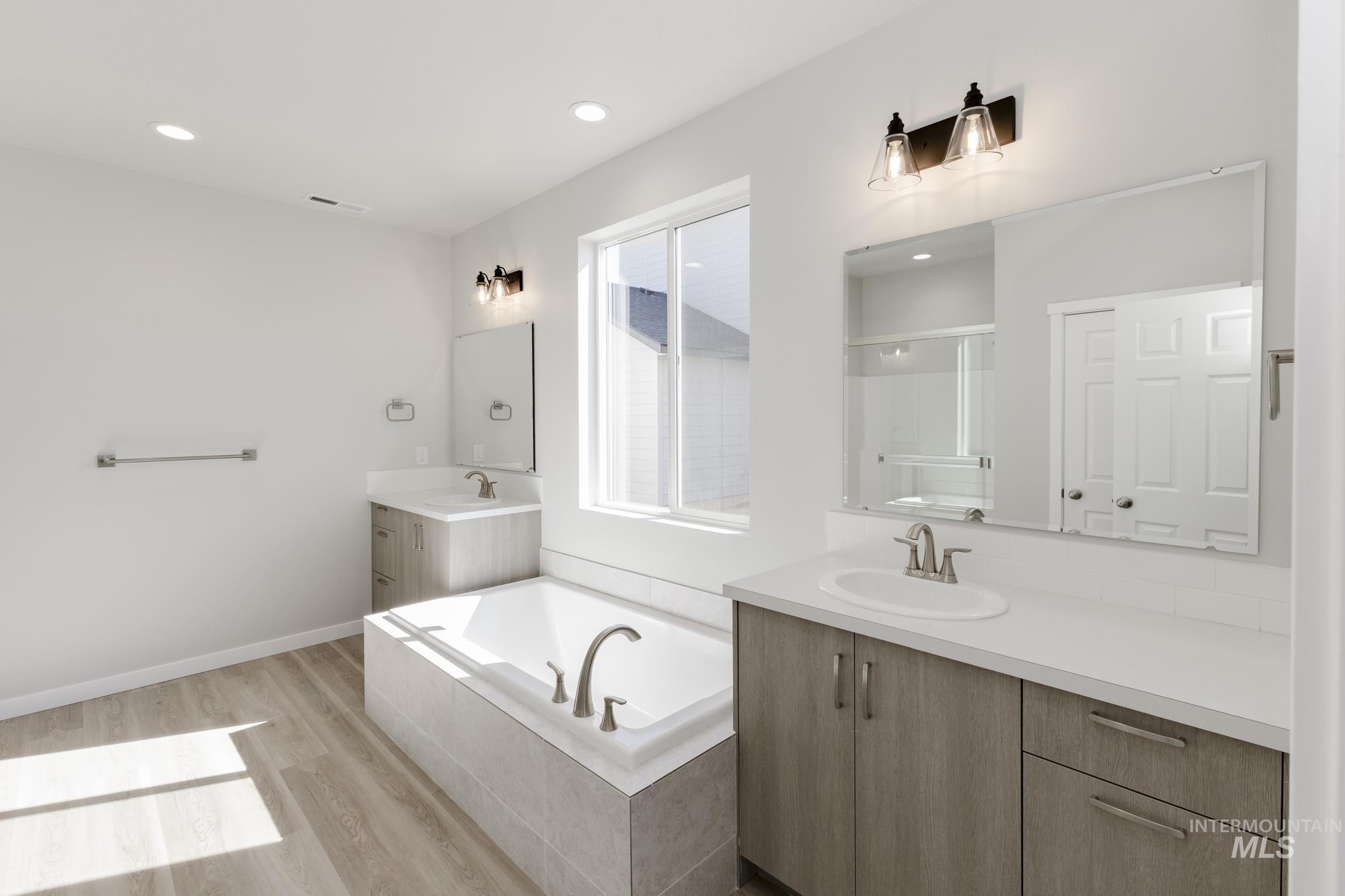 Bathroom with a garden tub, two vanities, a stall shower, light wood finished floors, and recessed lighting
