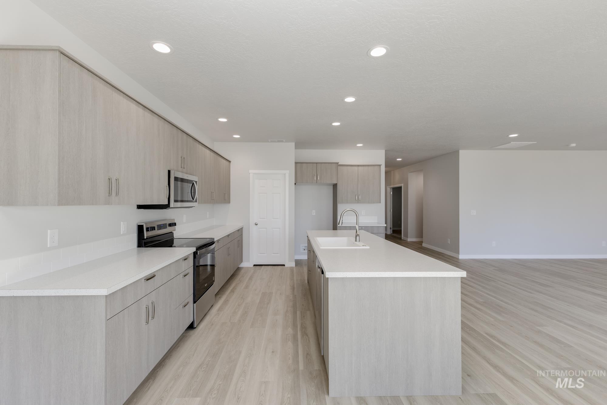 Kitchen featuring stainless steel appliances, modern cabinets, an island with sink, light wood-style floors, and recessed lighting