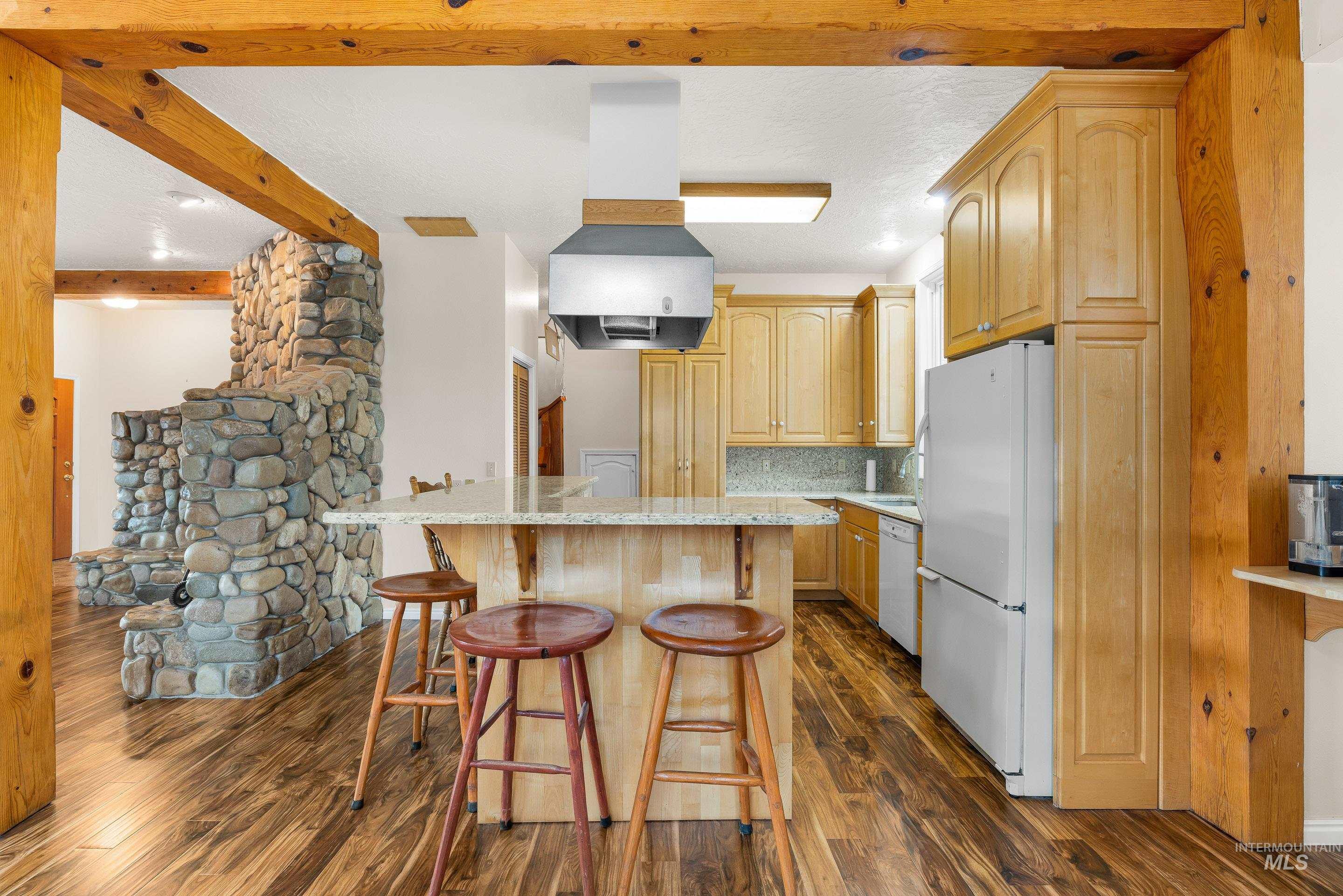 Kitchen featuring a kitchen breakfast bar, white appliances, light brown cabinets, backsplash, and dark wood-style floors