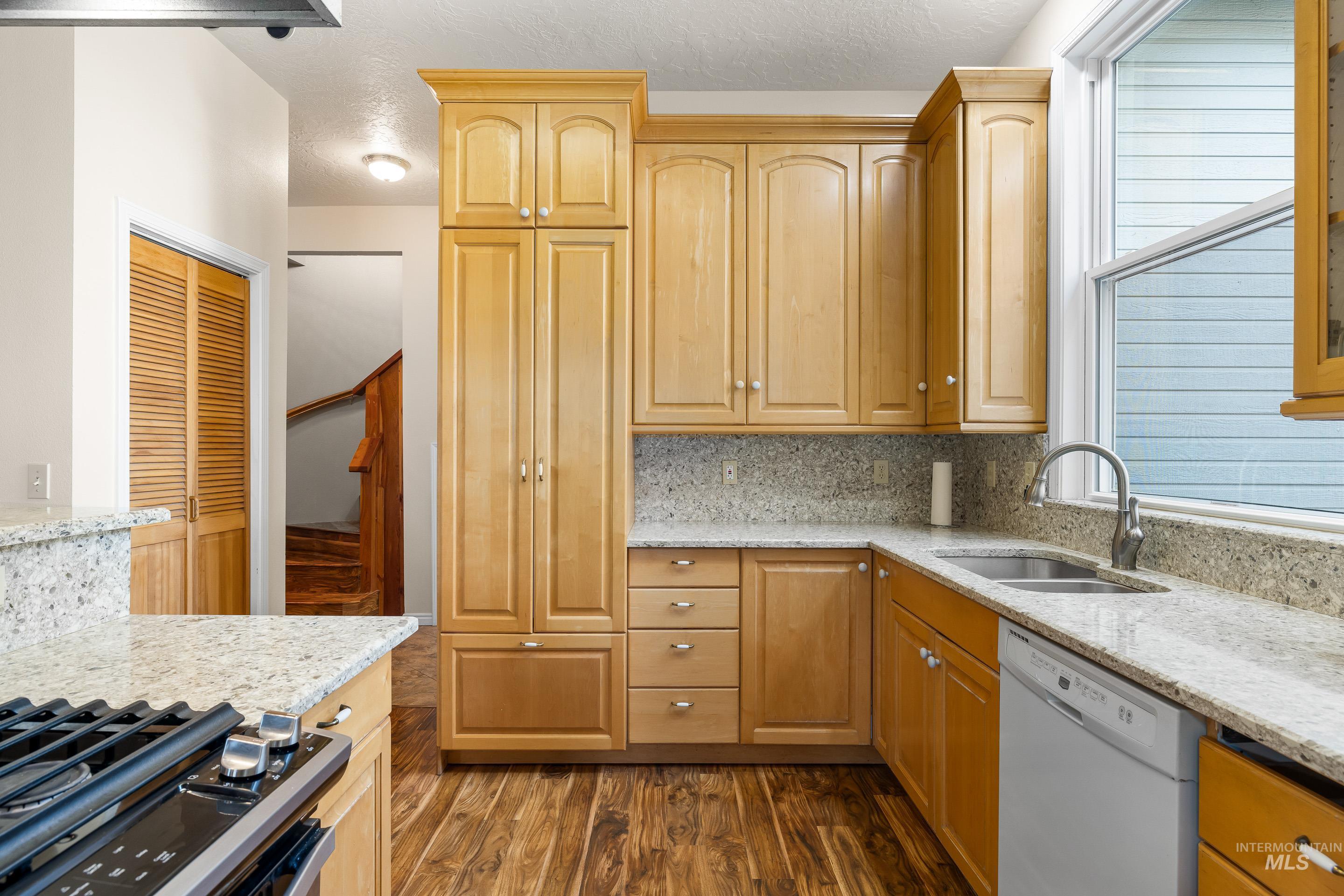 Kitchen with light stone counters, backsplash, dishwasher, and gas stove
