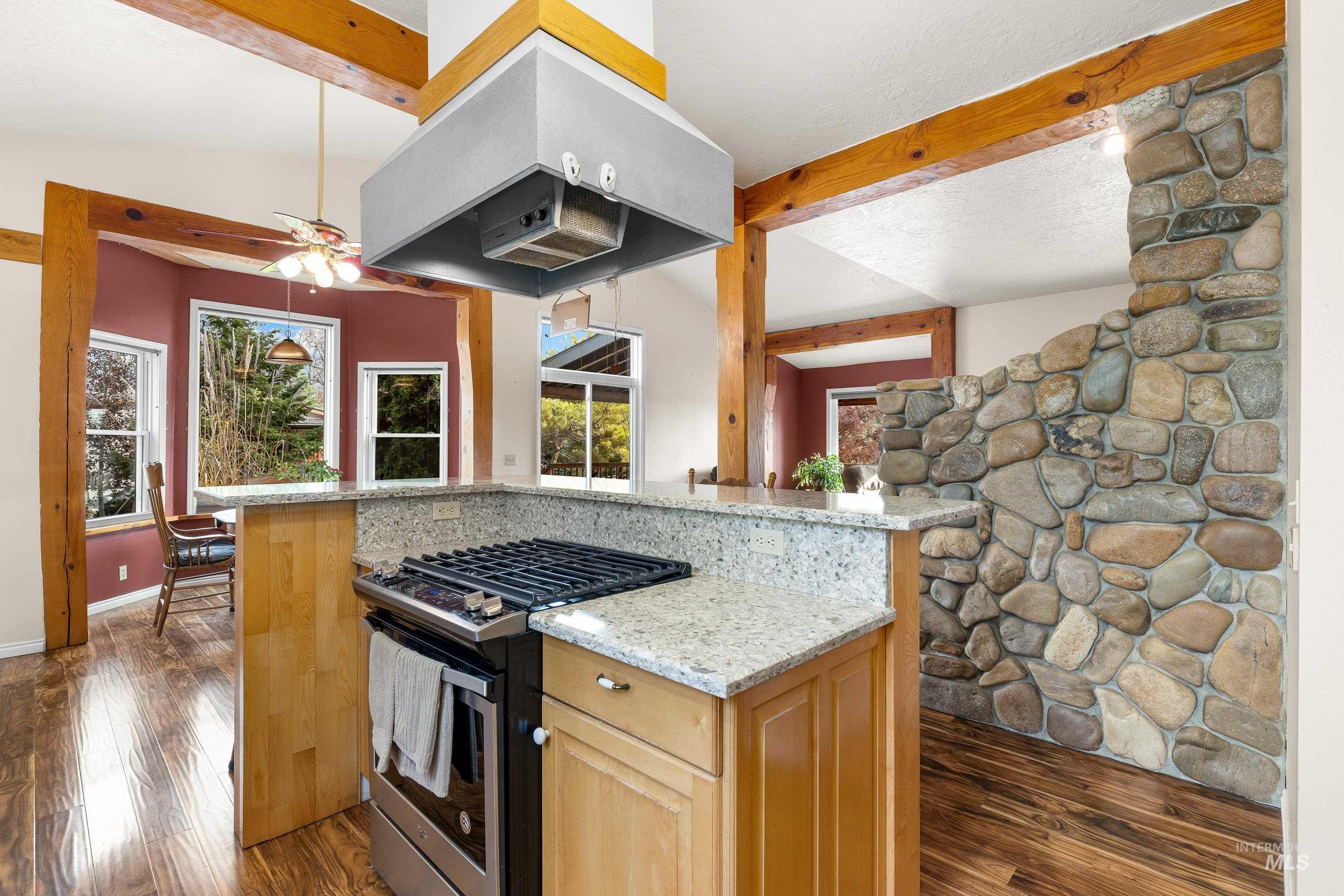 Kitchen featuring stainless steel gas stove, light stone counters, island range hood, and dark wood-style floors