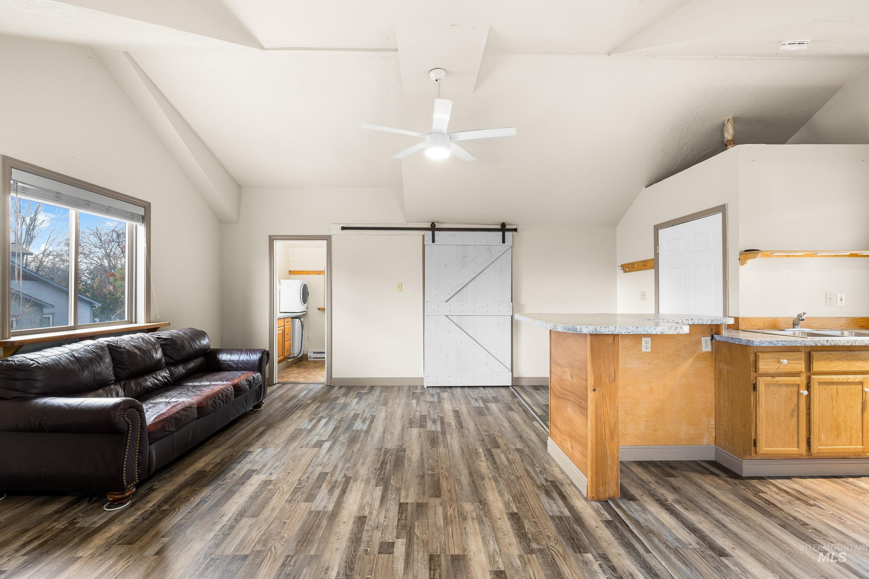 Living room featuring lofted ceiling, a barn door, a ceiling fan, and light wood-style floors