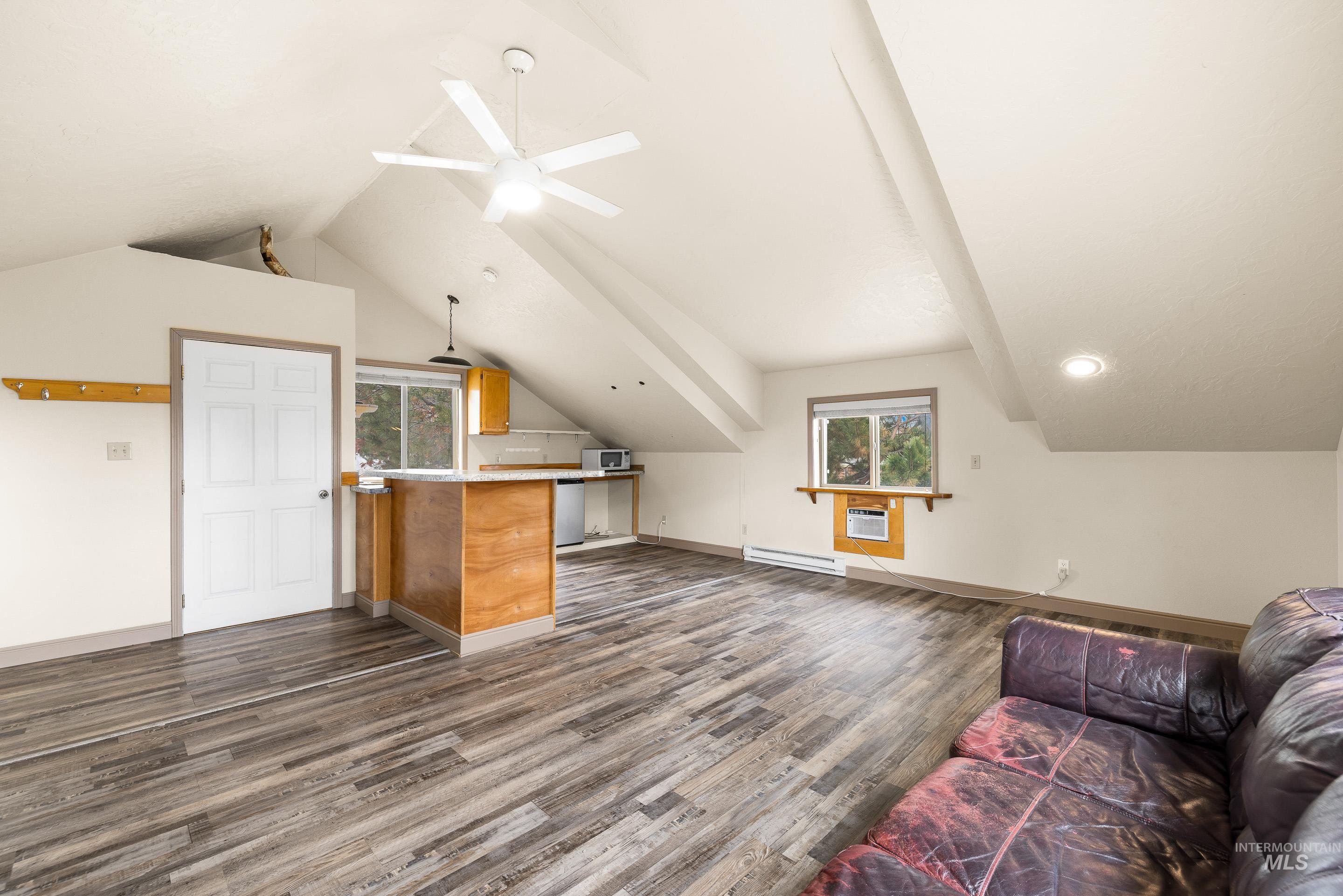 Additional living space with vaulted ceiling, dark wood-style flooring, baseboard heating, and ceiling fan