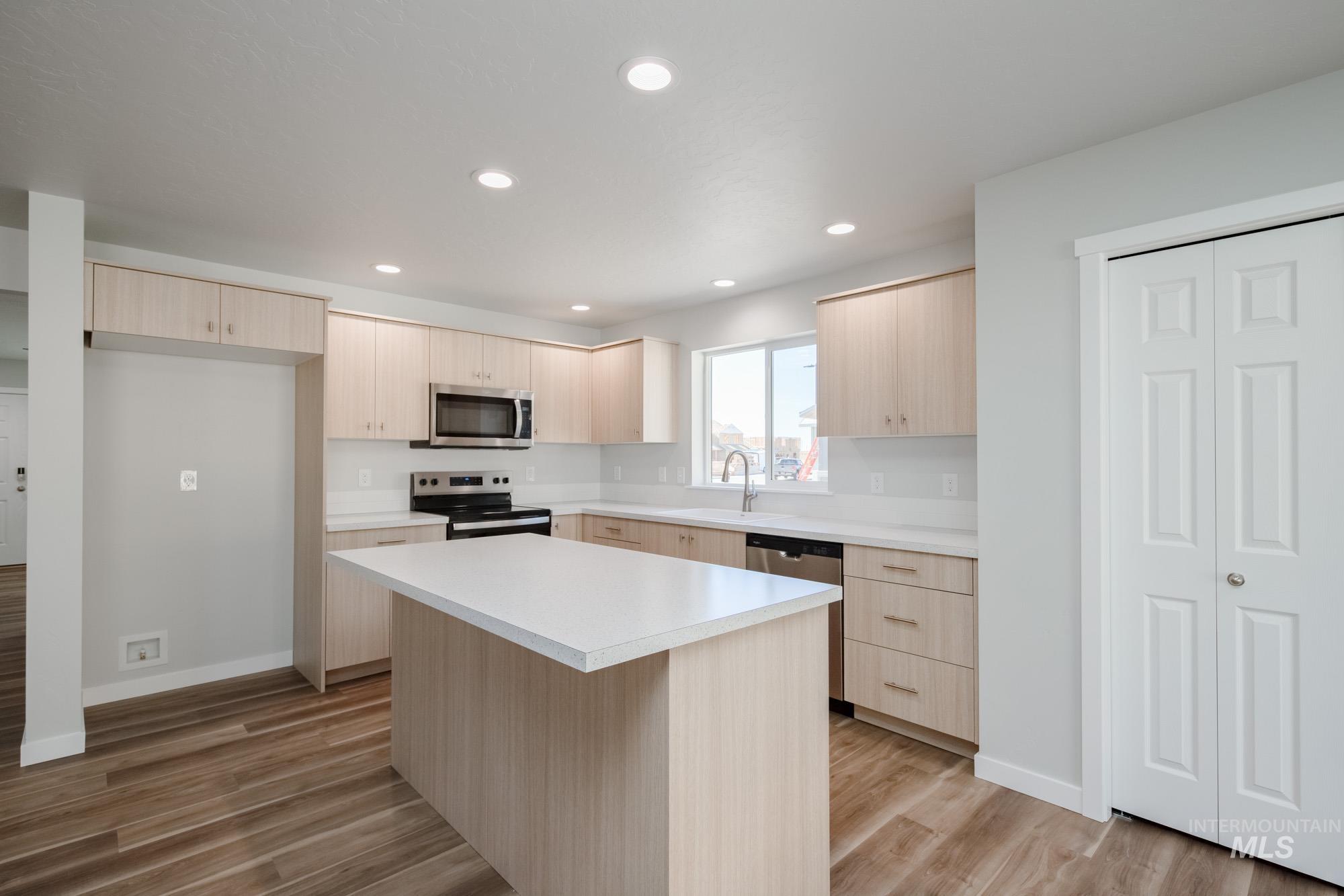 Kitchen with light brown cabinetry, light countertops, appliances with stainless steel finishes, dark wood-style flooring, and recessed lighting