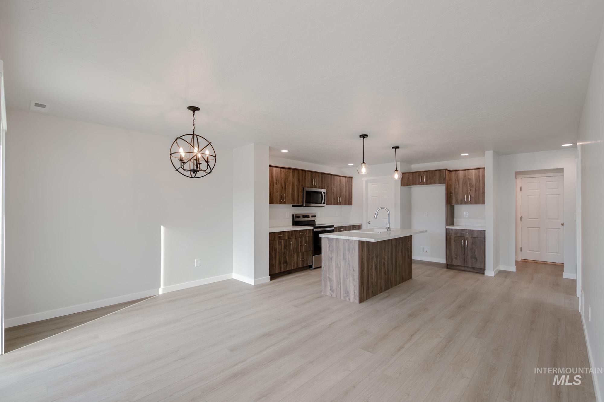 Kitchen with recessed lighting, pendant lighting, appliances with stainless steel finishes, an island with sink, and light wood finished floors