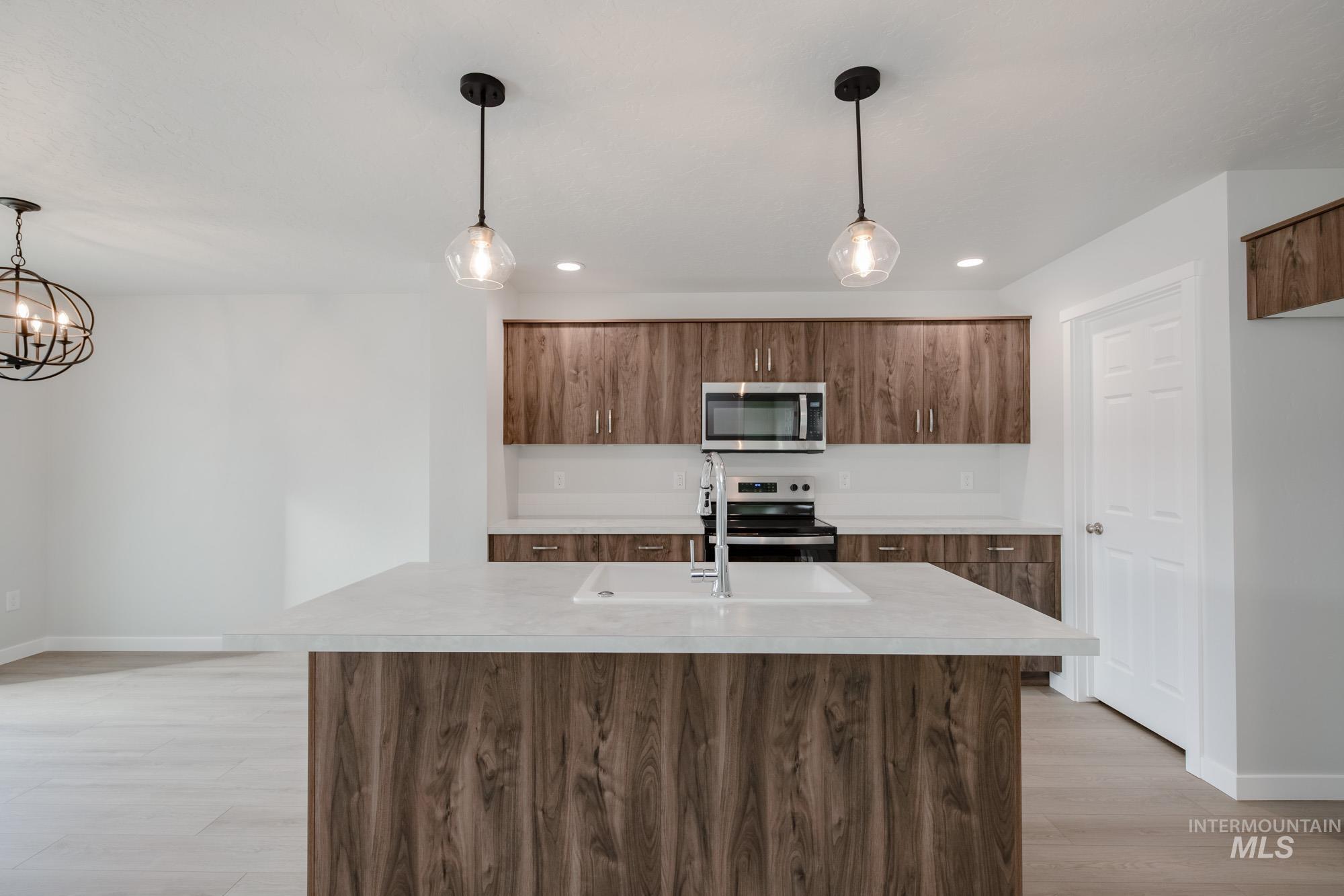 Kitchen featuring decorative light fixtures, light countertops, stainless steel appliances, light wood-style flooring, and an island with sink