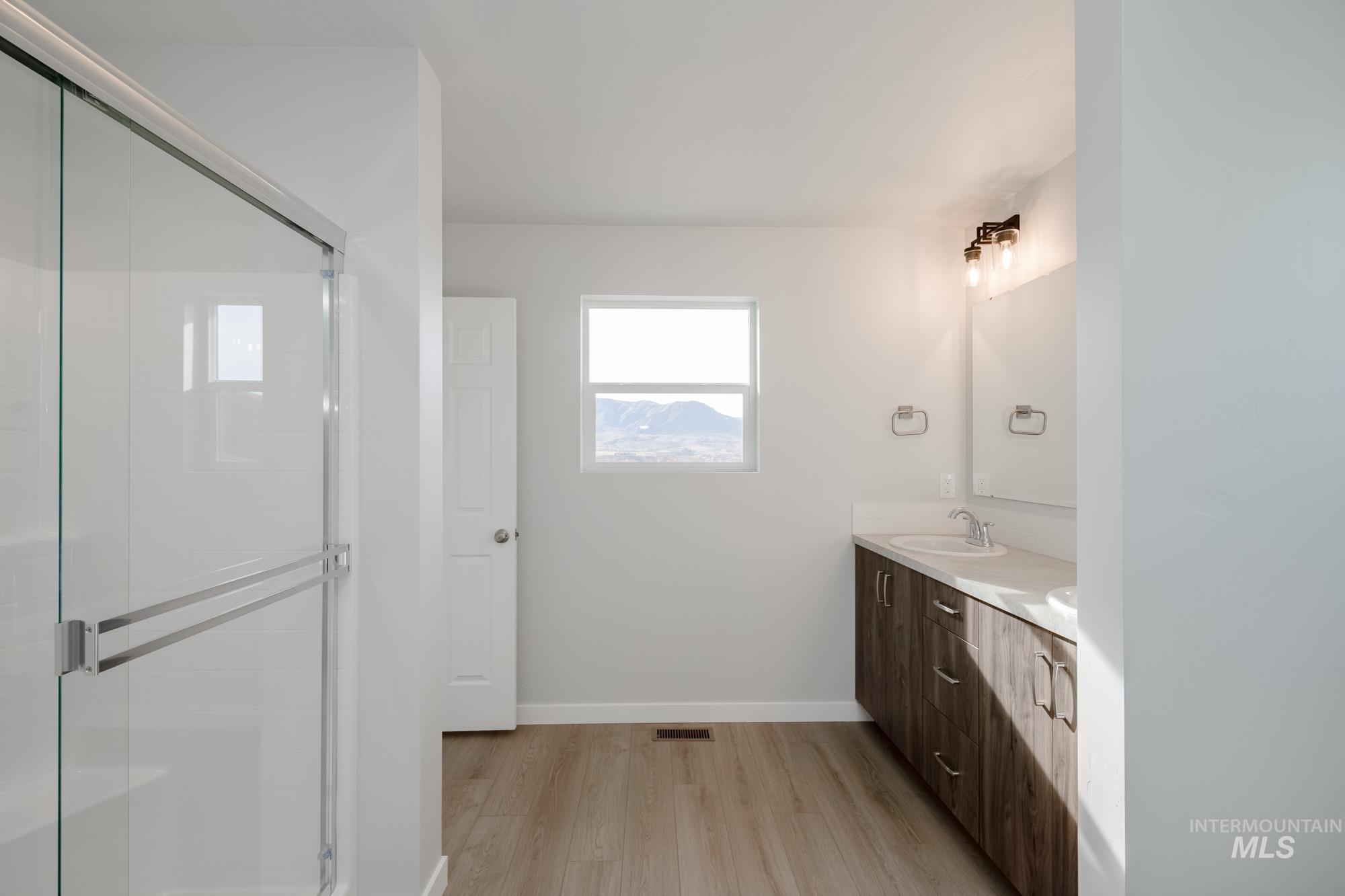 Full bathroom with light wood-style floors, double vanity, and a stall shower