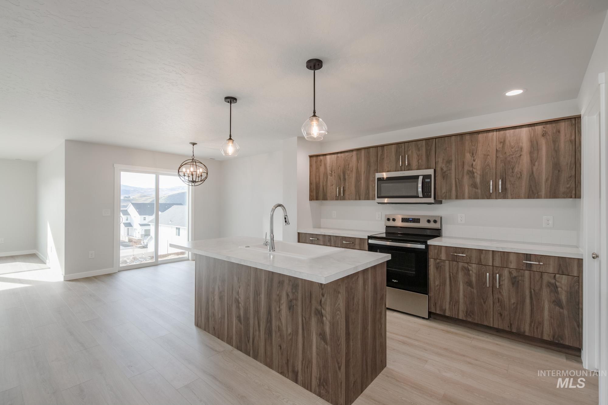 Kitchen with appliances with stainless steel finishes, light countertops, hanging light fixtures, an island with sink, and light wood finished floors