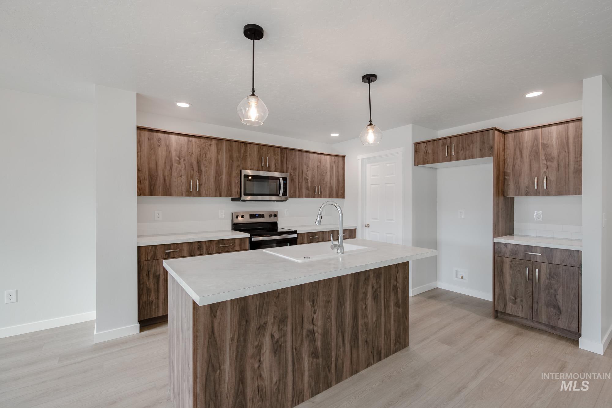 Kitchen featuring light countertops, appliances with stainless steel finishes, hanging light fixtures, light wood-style floors, and recessed lighting