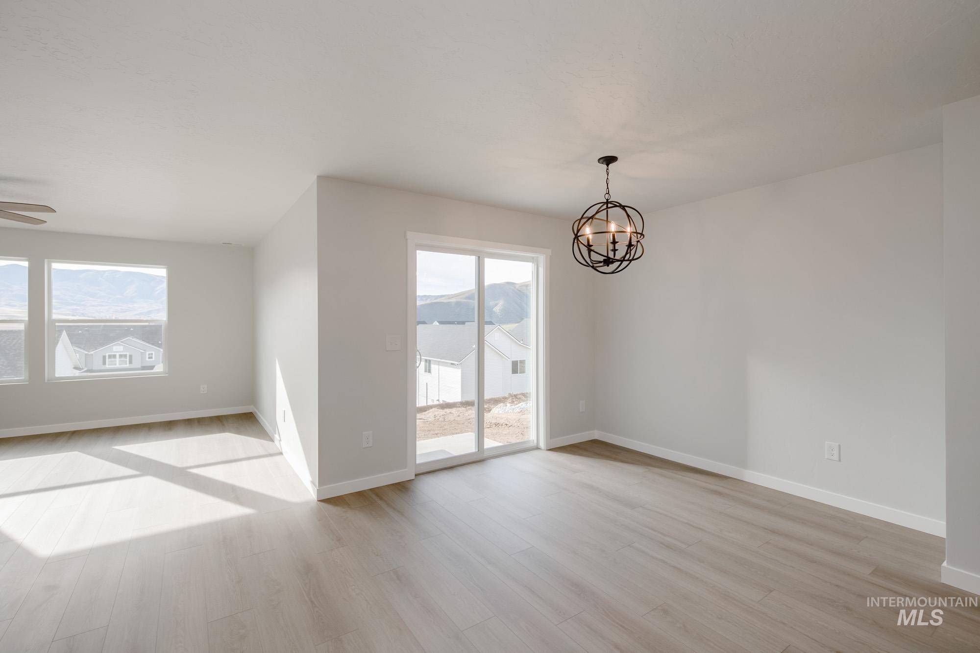 Empty room with light wood-type flooring, plenty of natural light, and a chandelier