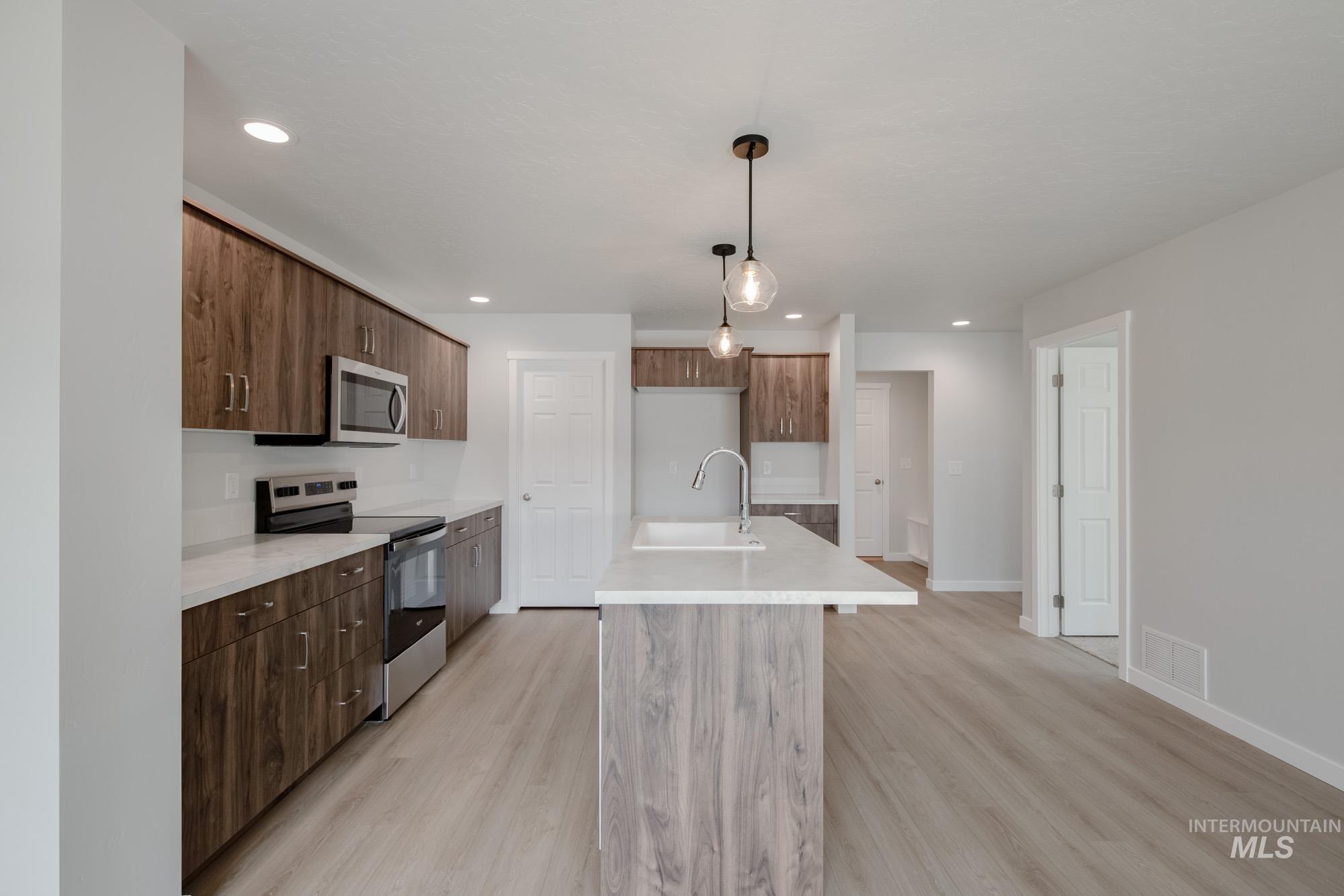 Kitchen featuring stainless steel appliances, a center island with sink, pendant lighting, light wood-style flooring, and recessed lighting