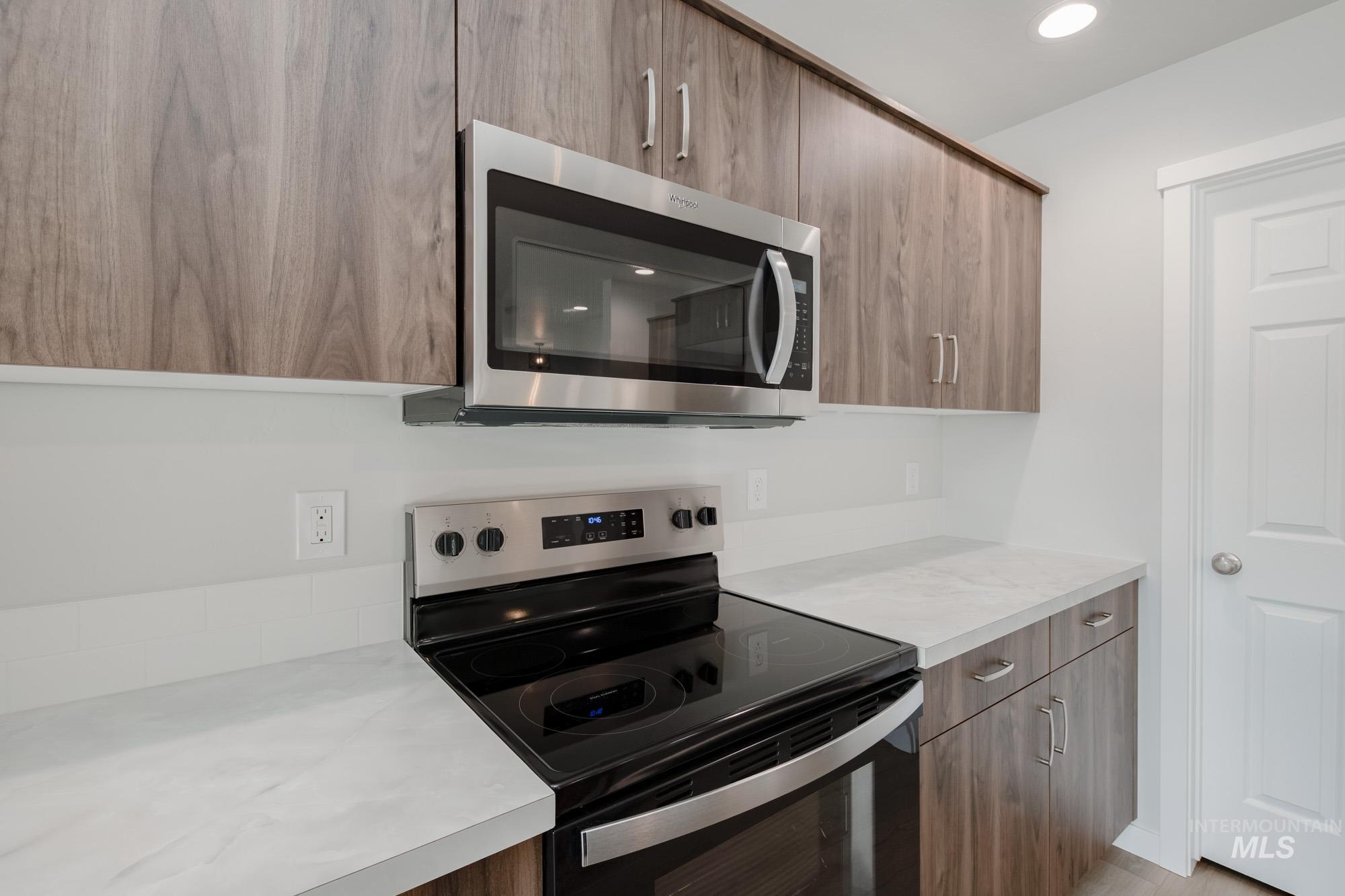 Kitchen featuring stainless steel appliances, modern cabinets, light countertops, recessed lighting, and brown cabinets
