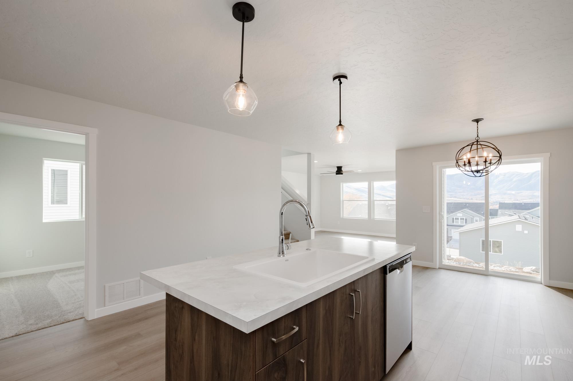 Kitchen with dark brown cabinetry, light countertops, decorative light fixtures, a ceiling fan, and light wood-style flooring