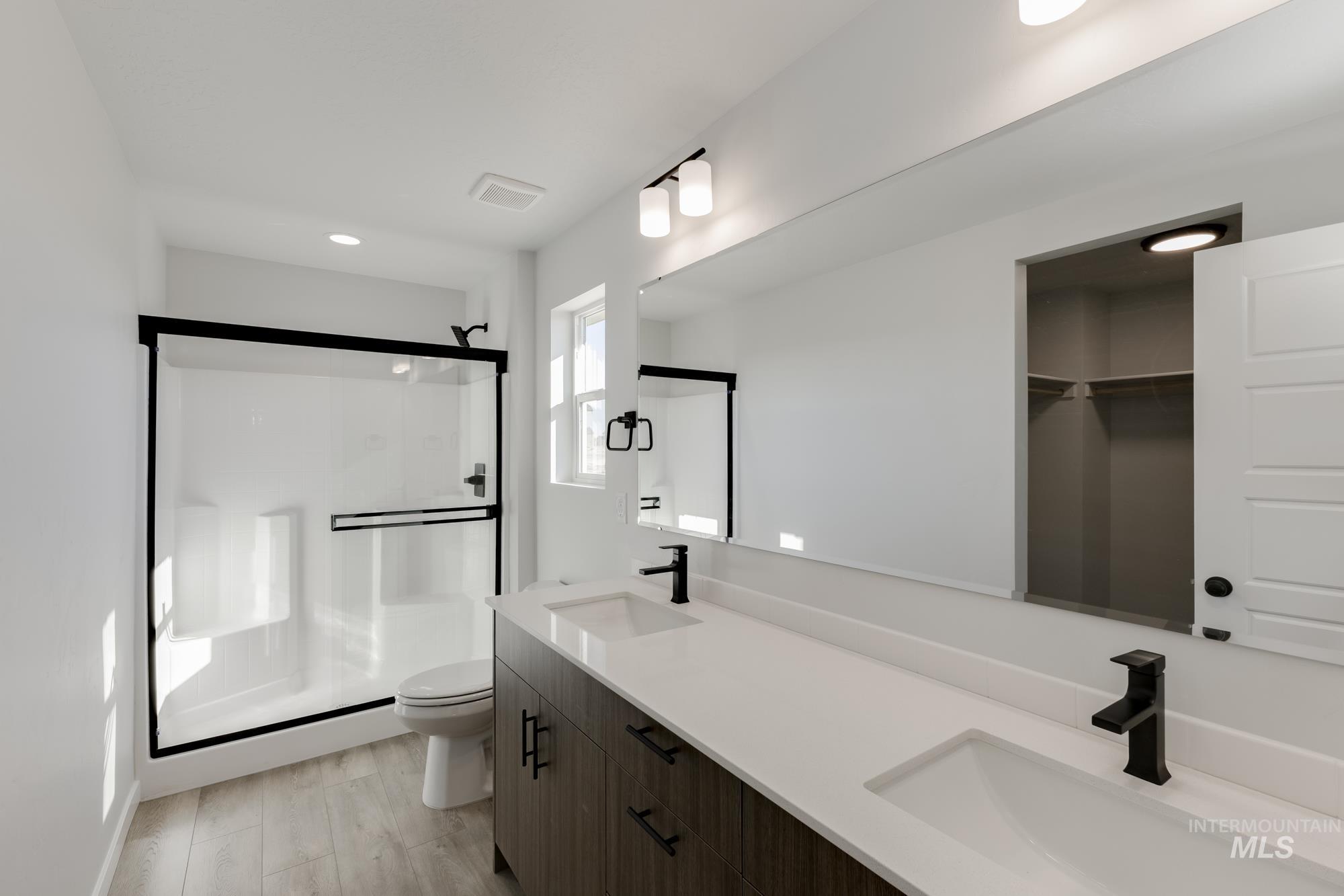 Bathroom featuring double vanity, a stall shower, light wood-style flooring, recessed lighting, and a spacious closet
