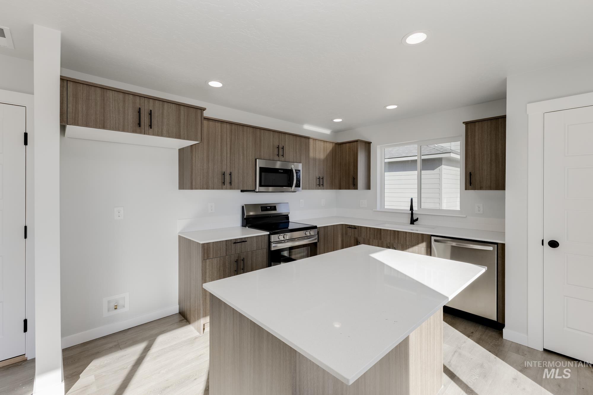 Kitchen featuring appliances with stainless steel finishes, light wood-type flooring, modern cabinets, light stone counters, and a center island