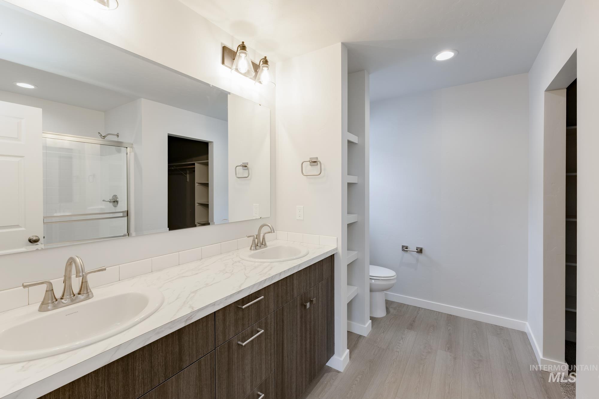 Full bath featuring a spacious closet, recessed lighting, a stall shower, double vanity, and light wood-style flooring