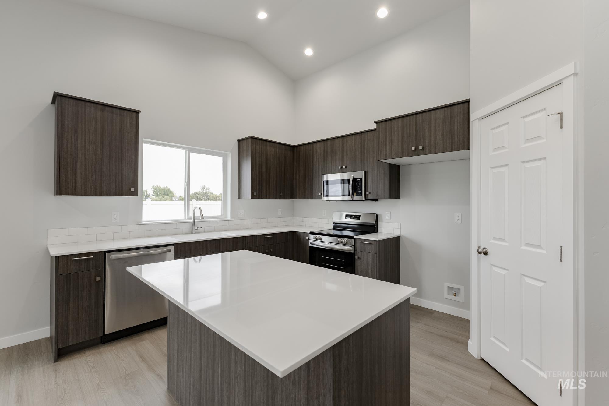 Kitchen featuring dark brown cabinets, stainless steel appliances, modern cabinets, light wood finished floors, and high vaulted ceiling