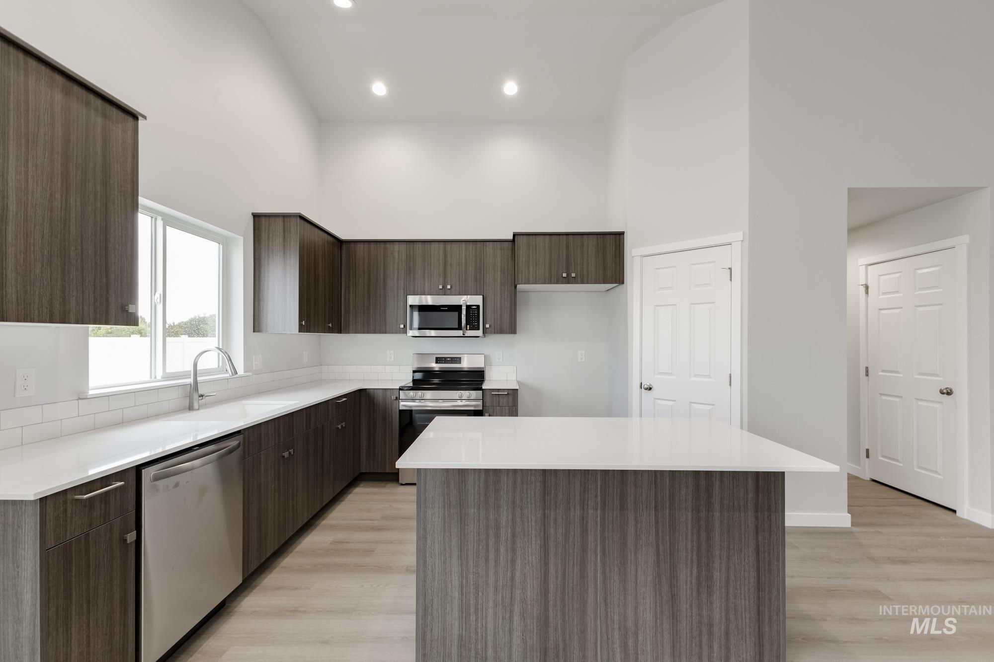 Kitchen featuring modern cabinets, dark brown cabinets, appliances with stainless steel finishes, a kitchen island, and light wood-style floors