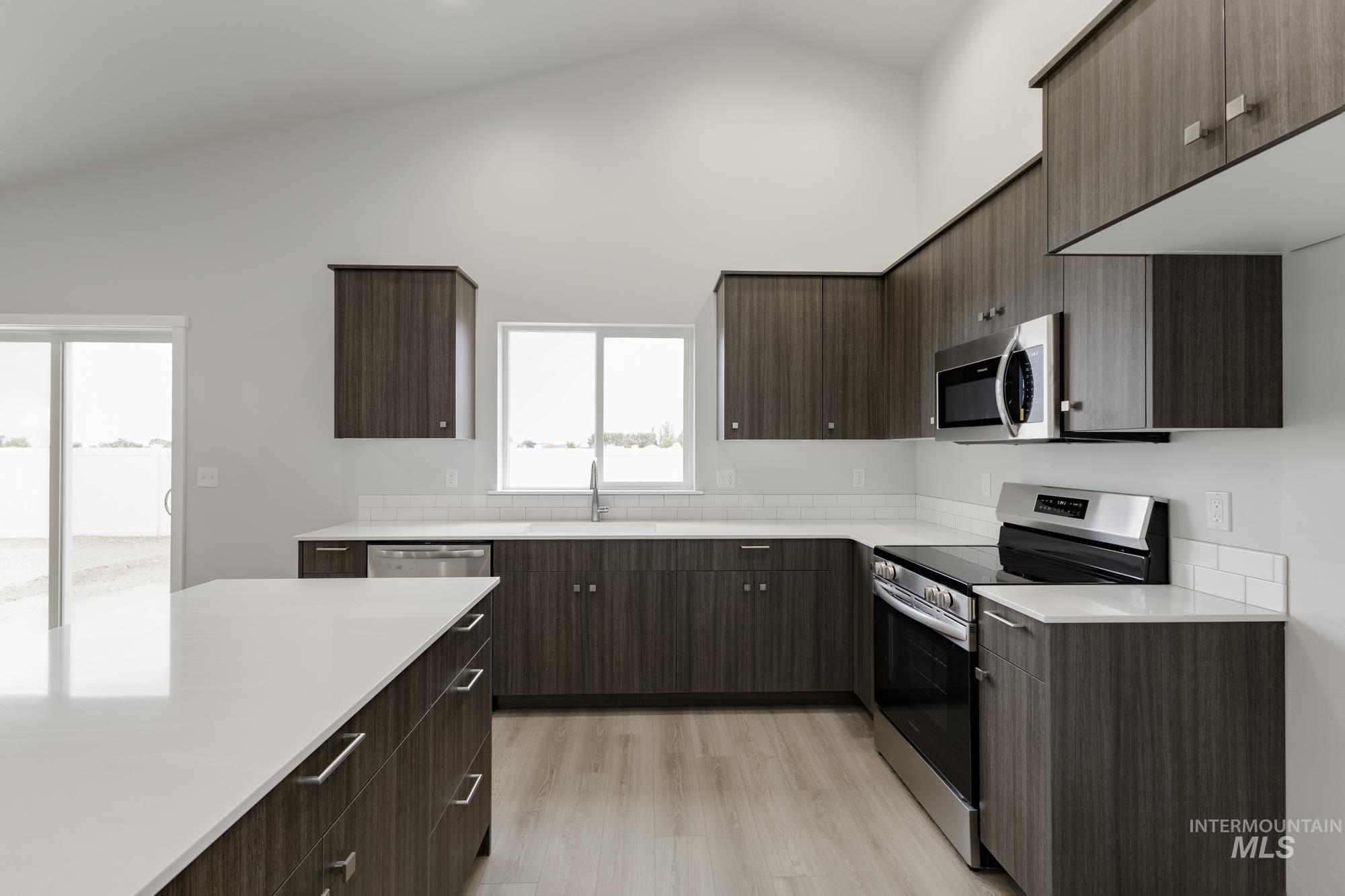 Kitchen featuring appliances with stainless steel finishes, modern cabinets, dark brown cabinets, light wood finished floors, and high vaulted ceiling