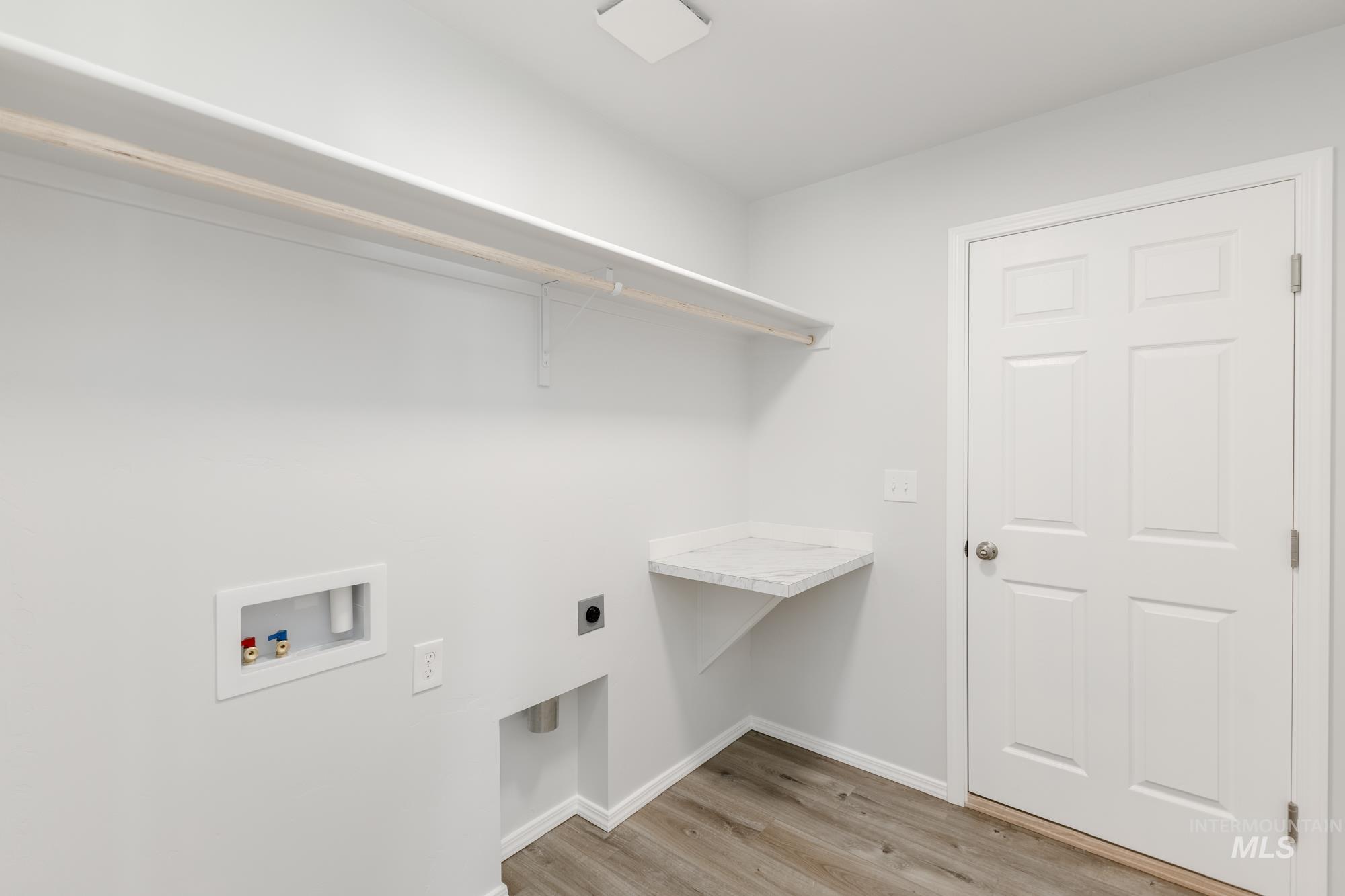 Laundry area with light wood-type flooring, hookup for a washing machine, and electric dryer hookup