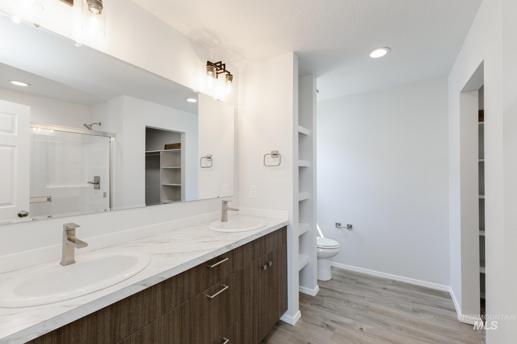 Full bathroom featuring a spacious closet, a stall shower, double vanity, light wood-style flooring, and recessed lighting