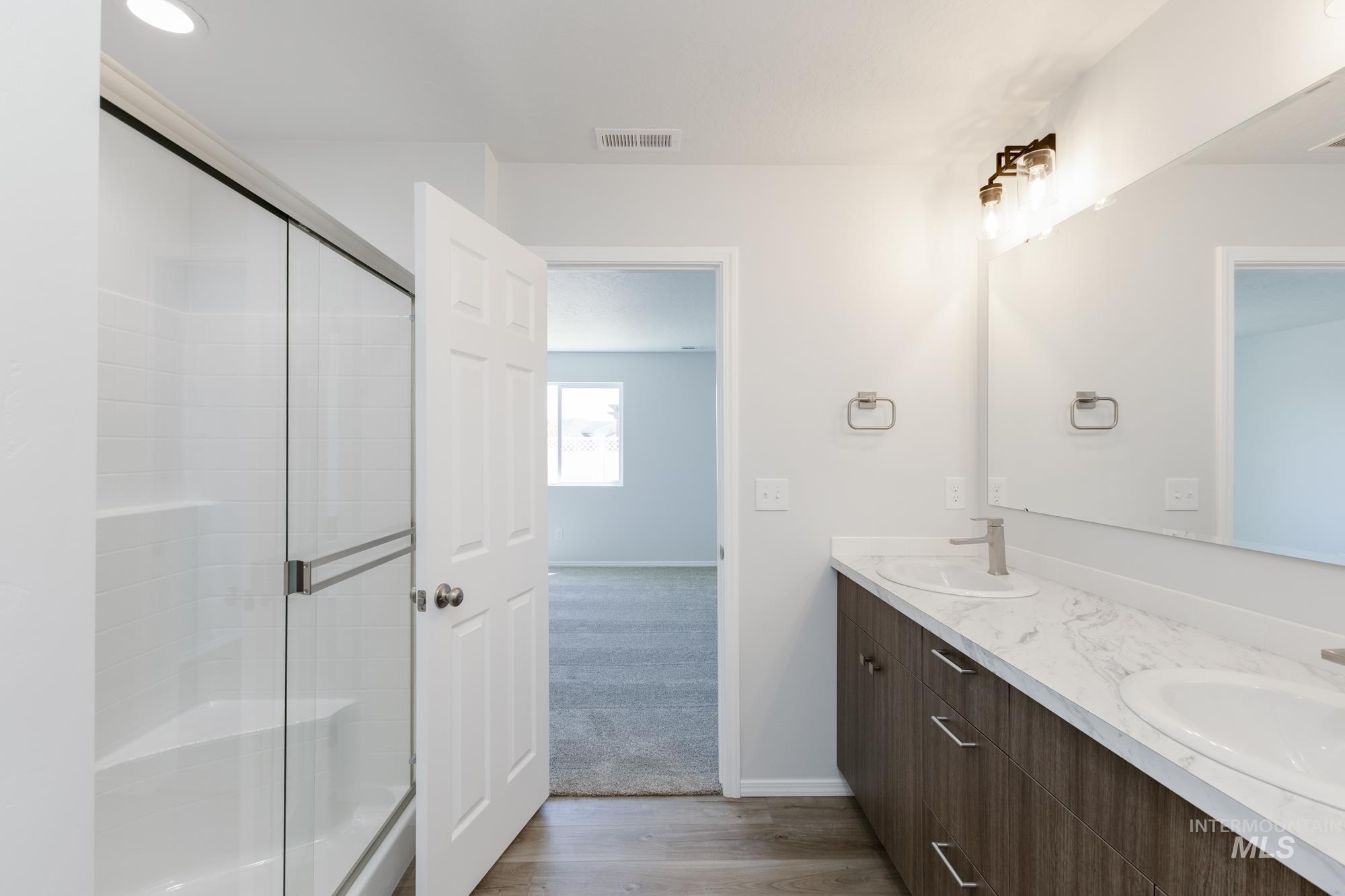 Full bathroom with light wood-type flooring, double vanity, a shower stall, and light carpet
