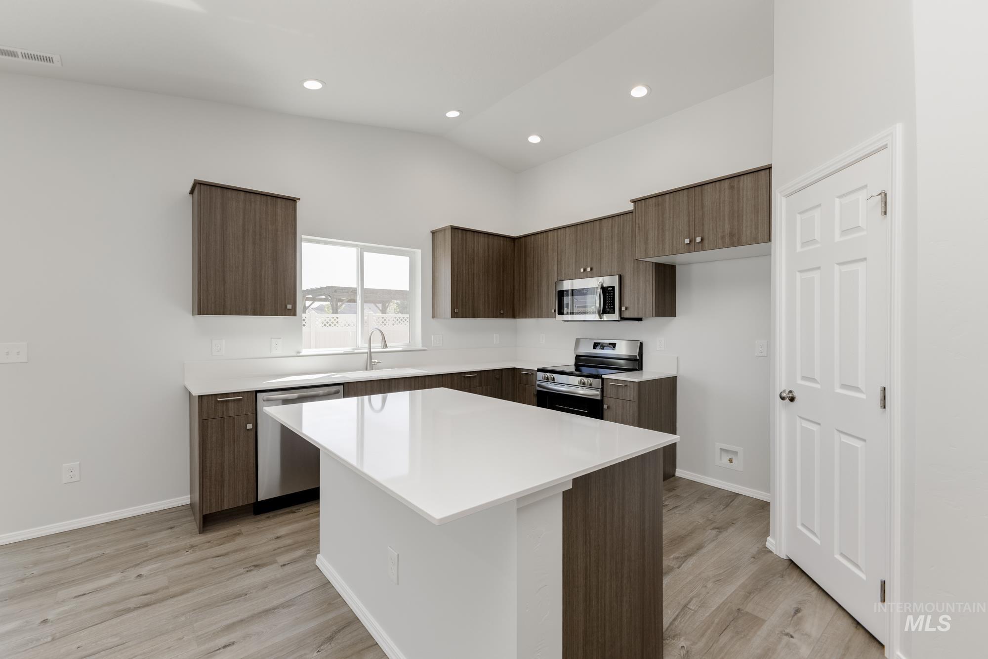 Kitchen with stainless steel appliances, modern cabinets, a center island, light wood finished floors, and vaulted ceiling