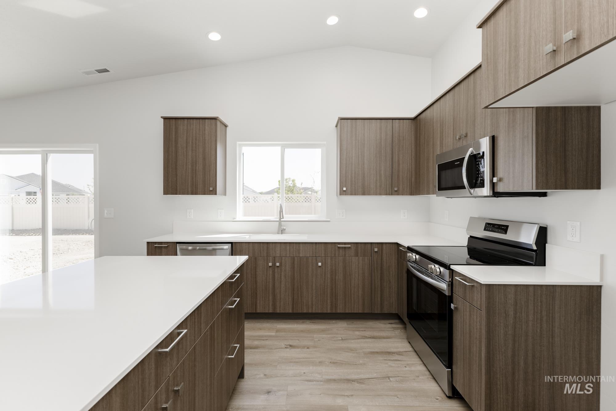 Kitchen featuring stainless steel appliances, modern cabinets, lofted ceiling, light wood-type flooring, and recessed lighting