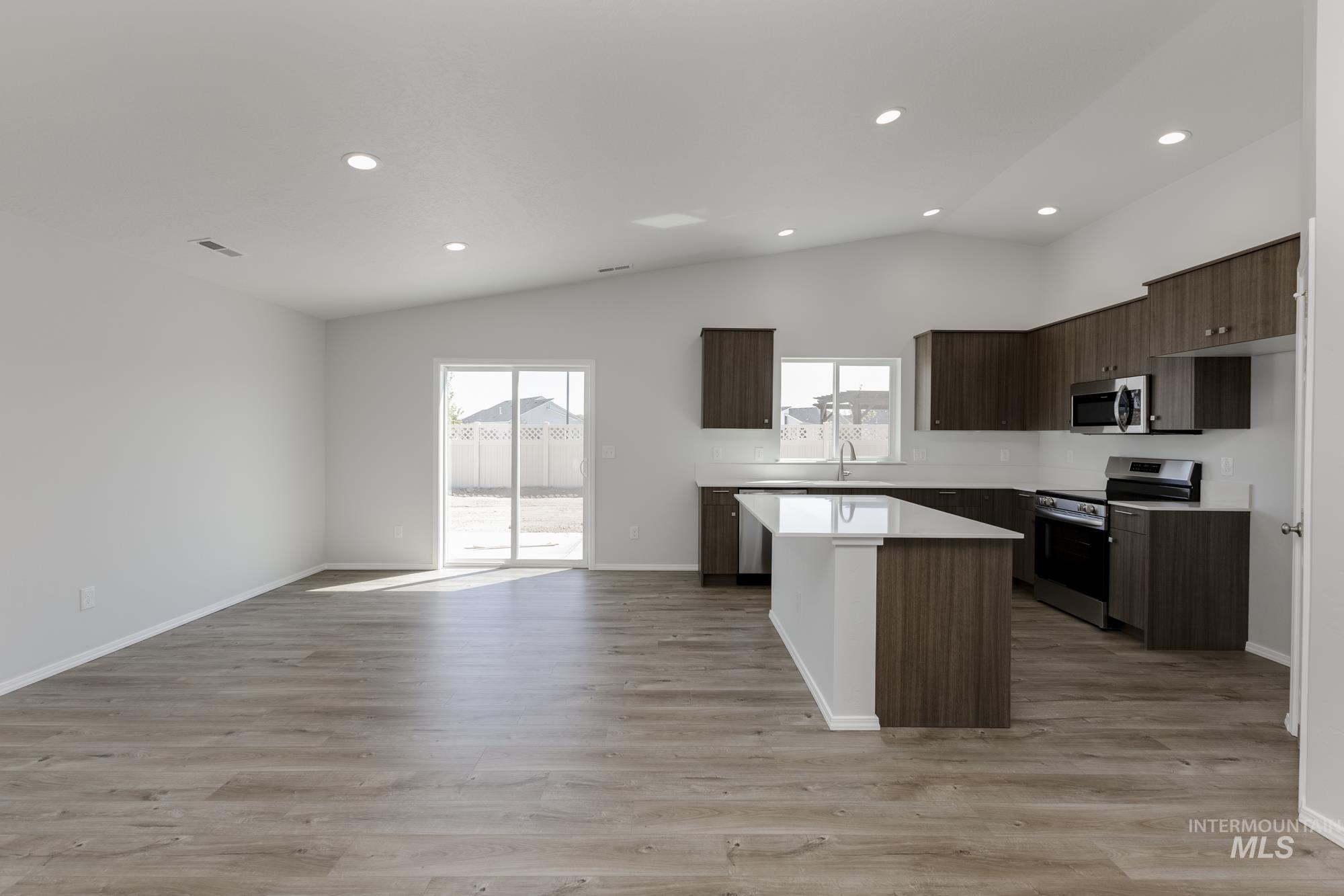 Kitchen with dark brown cabinetry, a kitchen island, stainless steel appliances, modern cabinets, and light wood finished floors