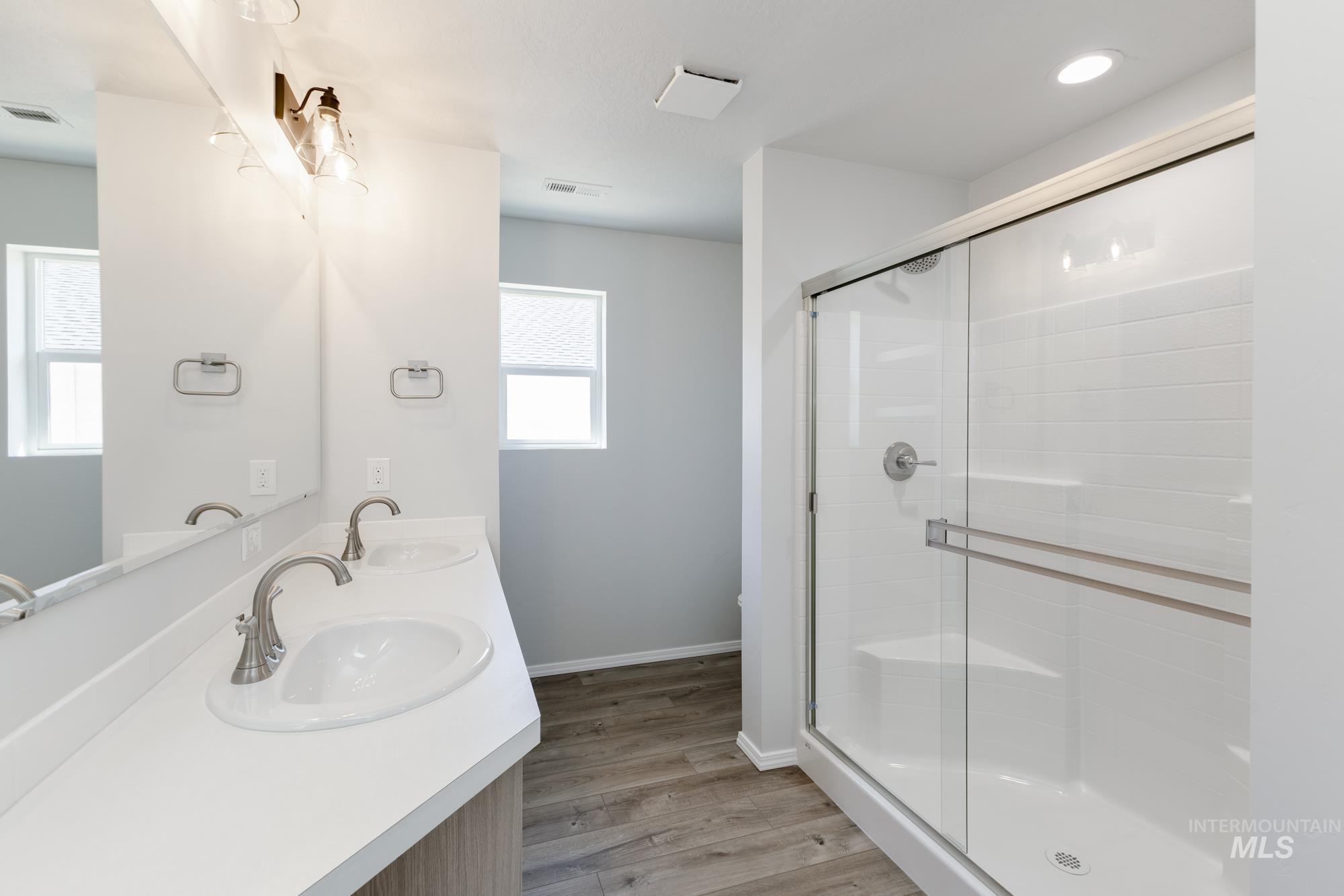 Full bath with light wood-style flooring, double vanity, and a shower stall
