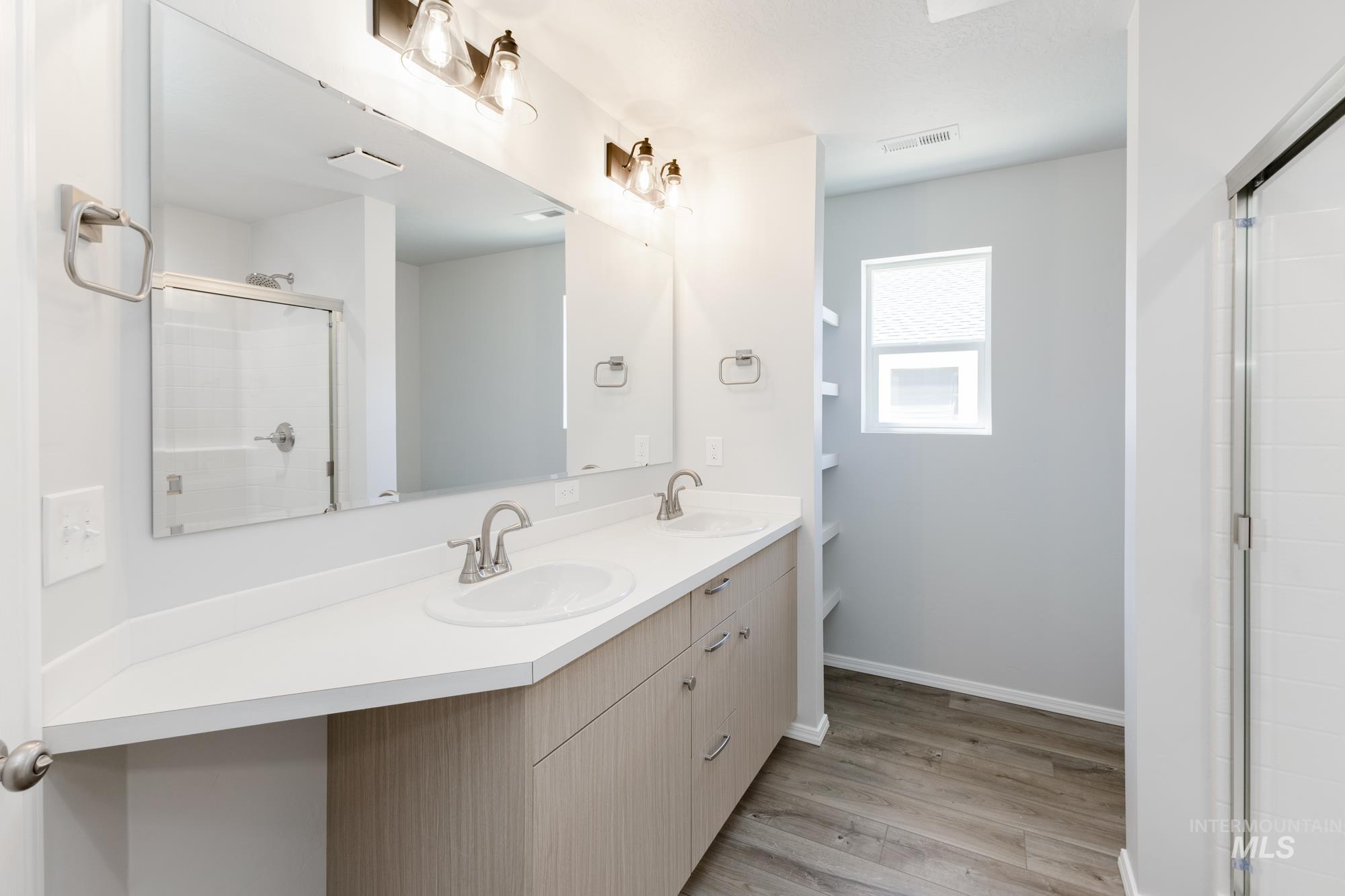 Full bathroom featuring light wood-type flooring, double vanity, and a stall shower