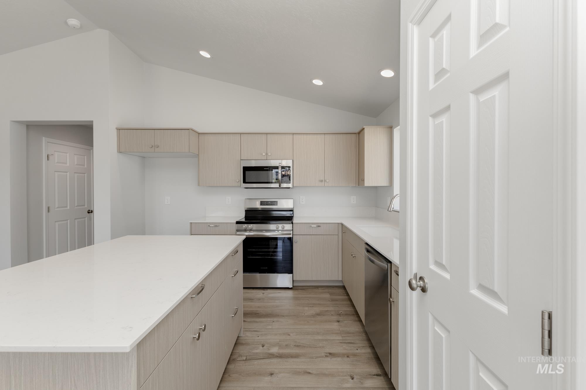 Kitchen featuring stainless steel appliances, light brown cabinets, lofted ceiling, modern cabinets, and light wood finished floors
