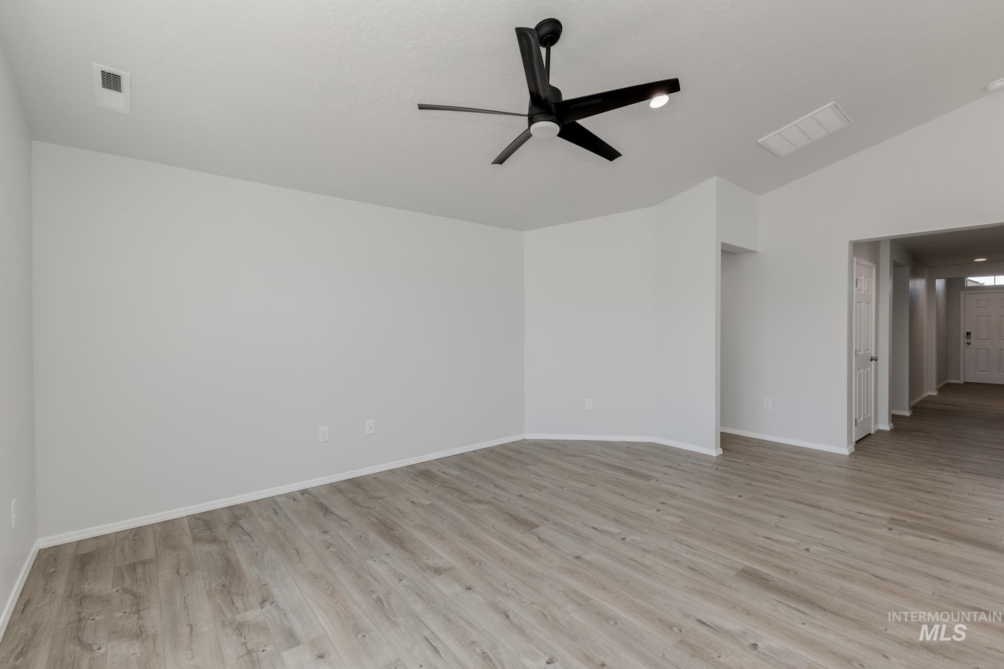 Empty room featuring light wood finished floors, lofted ceiling, and ceiling fan