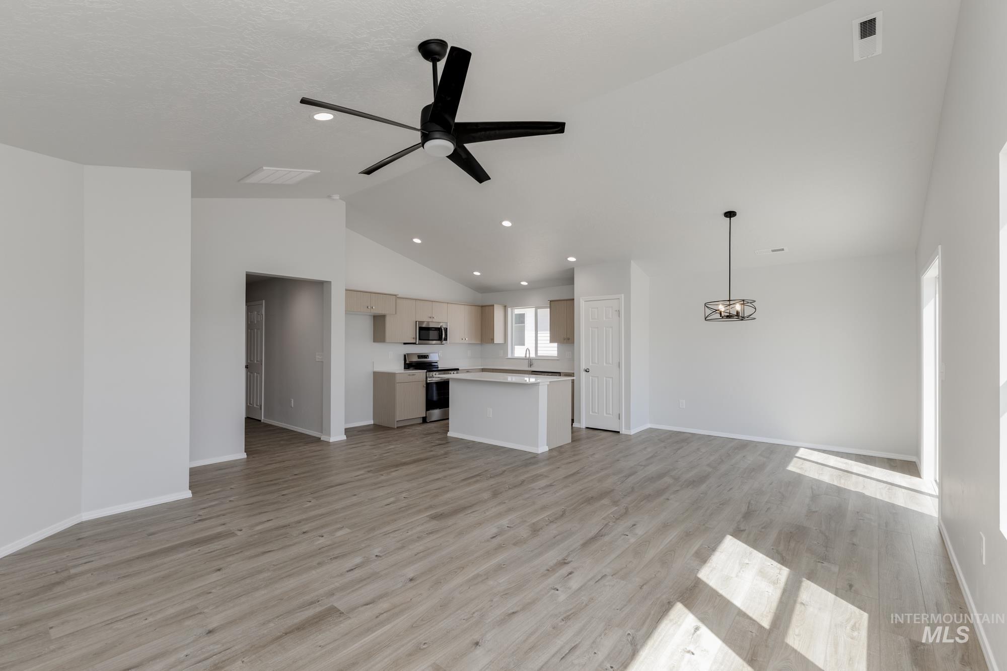 Unfurnished living room featuring lofted ceiling, light wood-style flooring, a ceiling fan, recessed lighting, and a chandelier