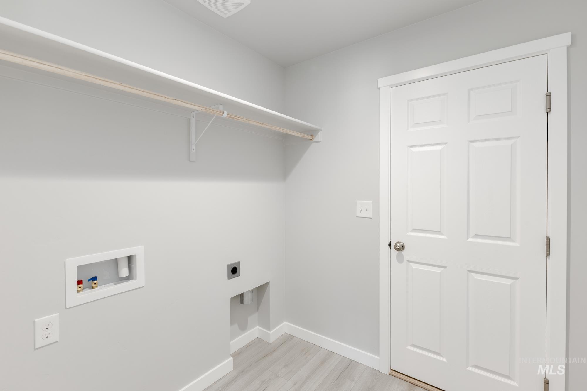 Washroom with hookup for an electric dryer, hookup for a washing machine, and light wood-style flooring