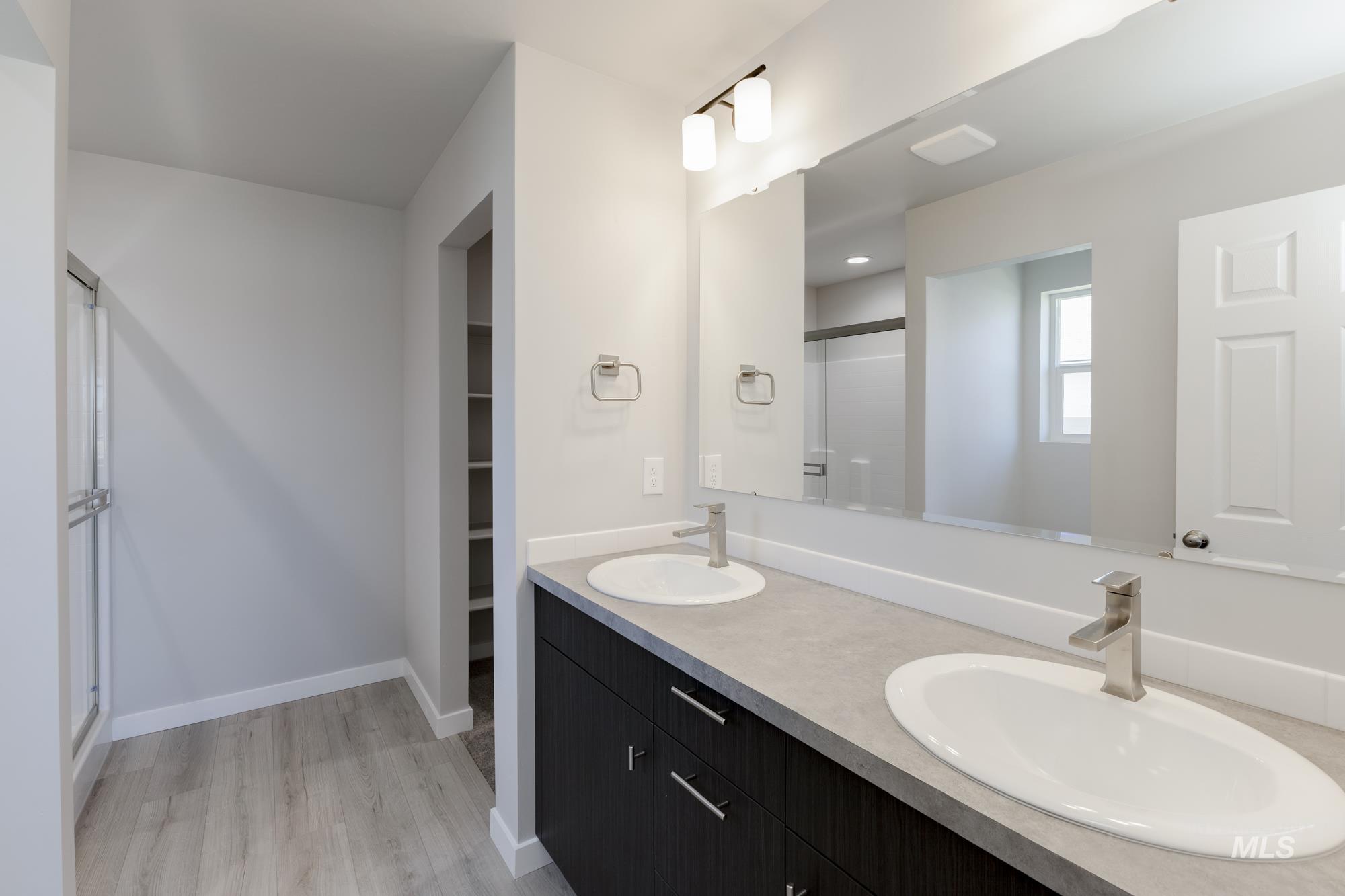 Full bath featuring a stall shower, double vanity, light wood-style flooring, and a spacious closet