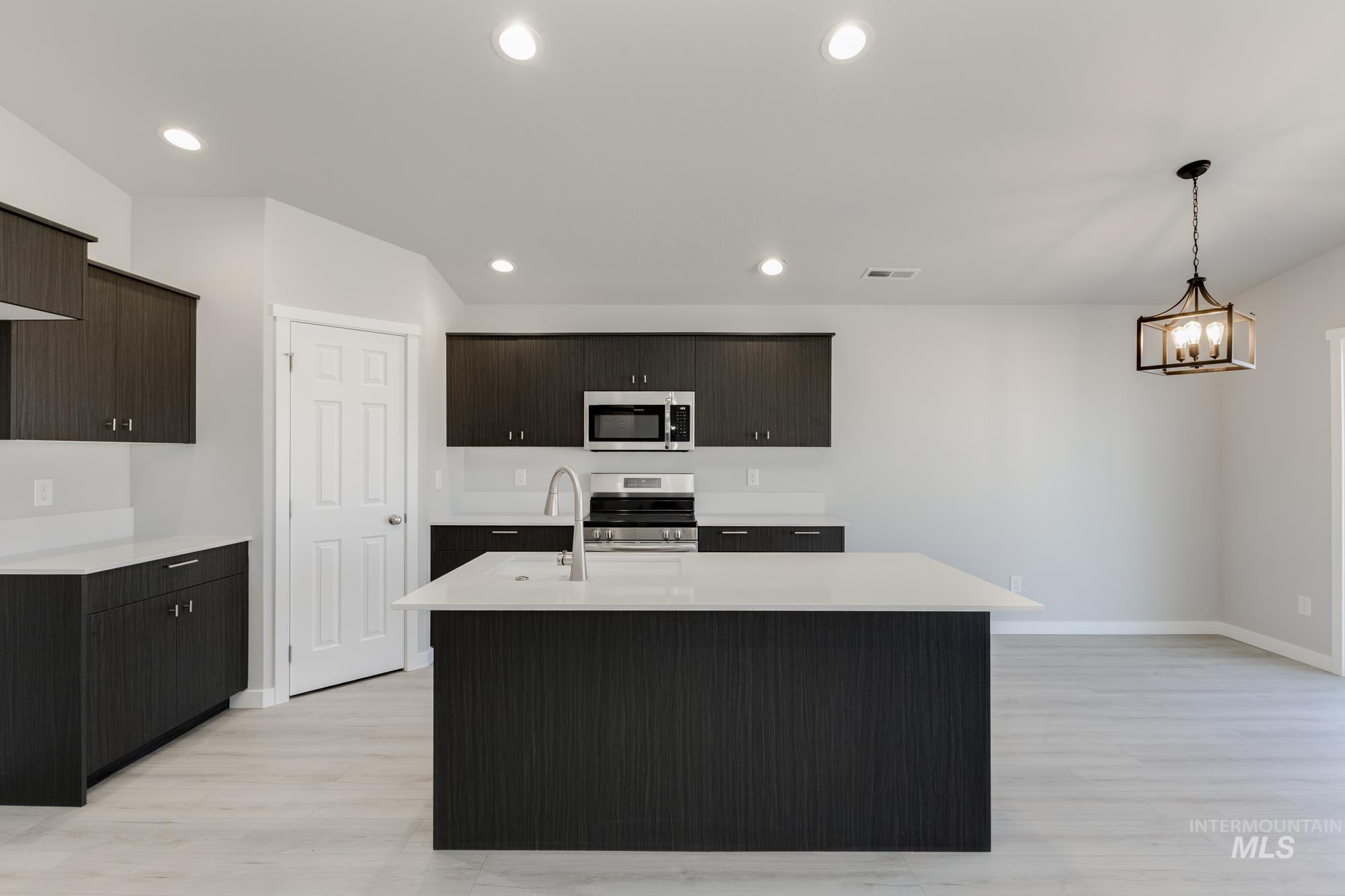 Kitchen with decorative light fixtures, appliances with stainless steel finishes, a center island with sink, light wood-type flooring, and recessed lighting