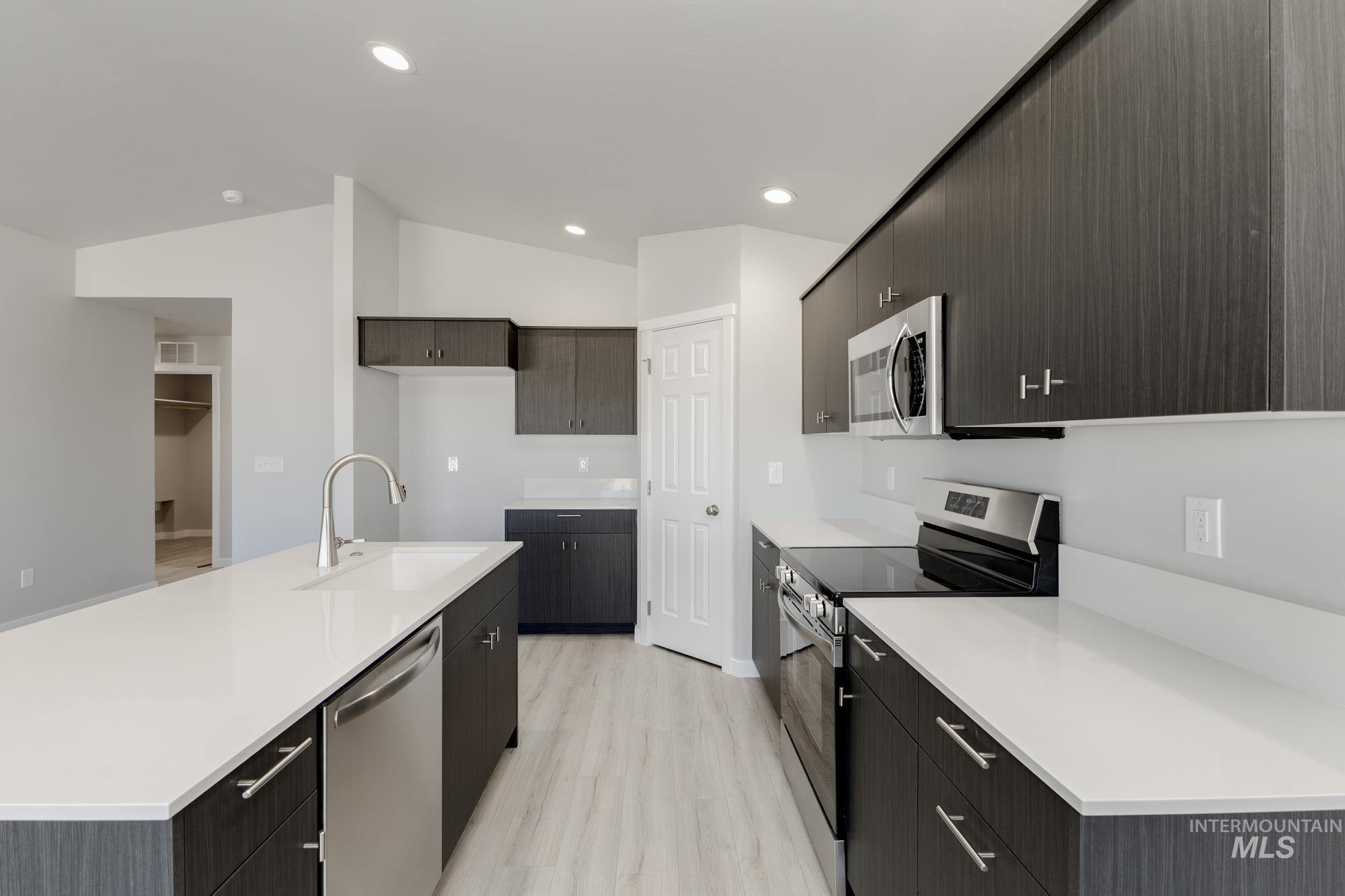 Kitchen with appliances with stainless steel finishes, light wood-type flooring, a kitchen island with sink, vaulted ceiling, and recessed lighting