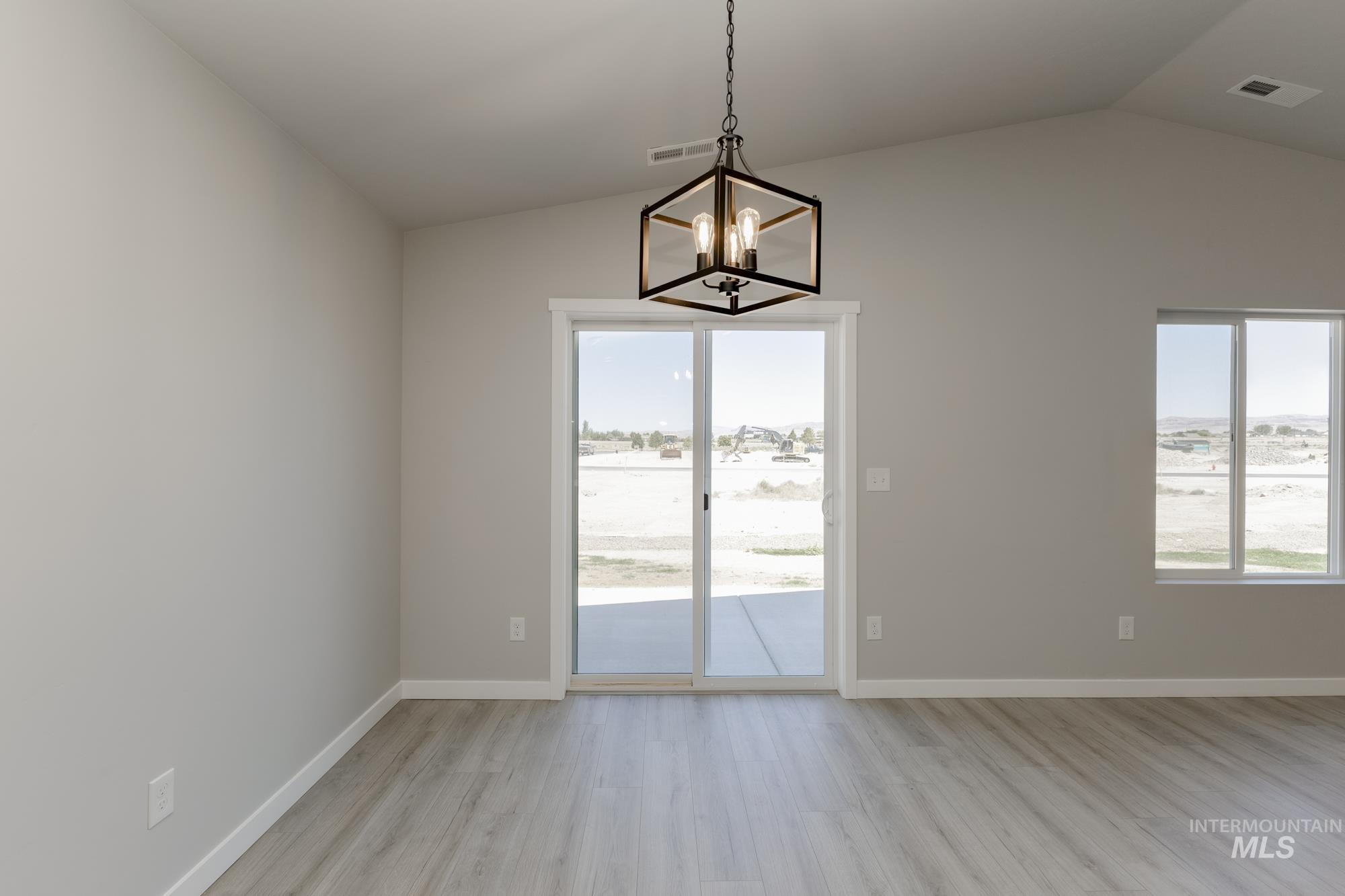 Unfurnished dining area with light wood-type flooring, healthy amount of natural light, vaulted ceiling, and a chandelier