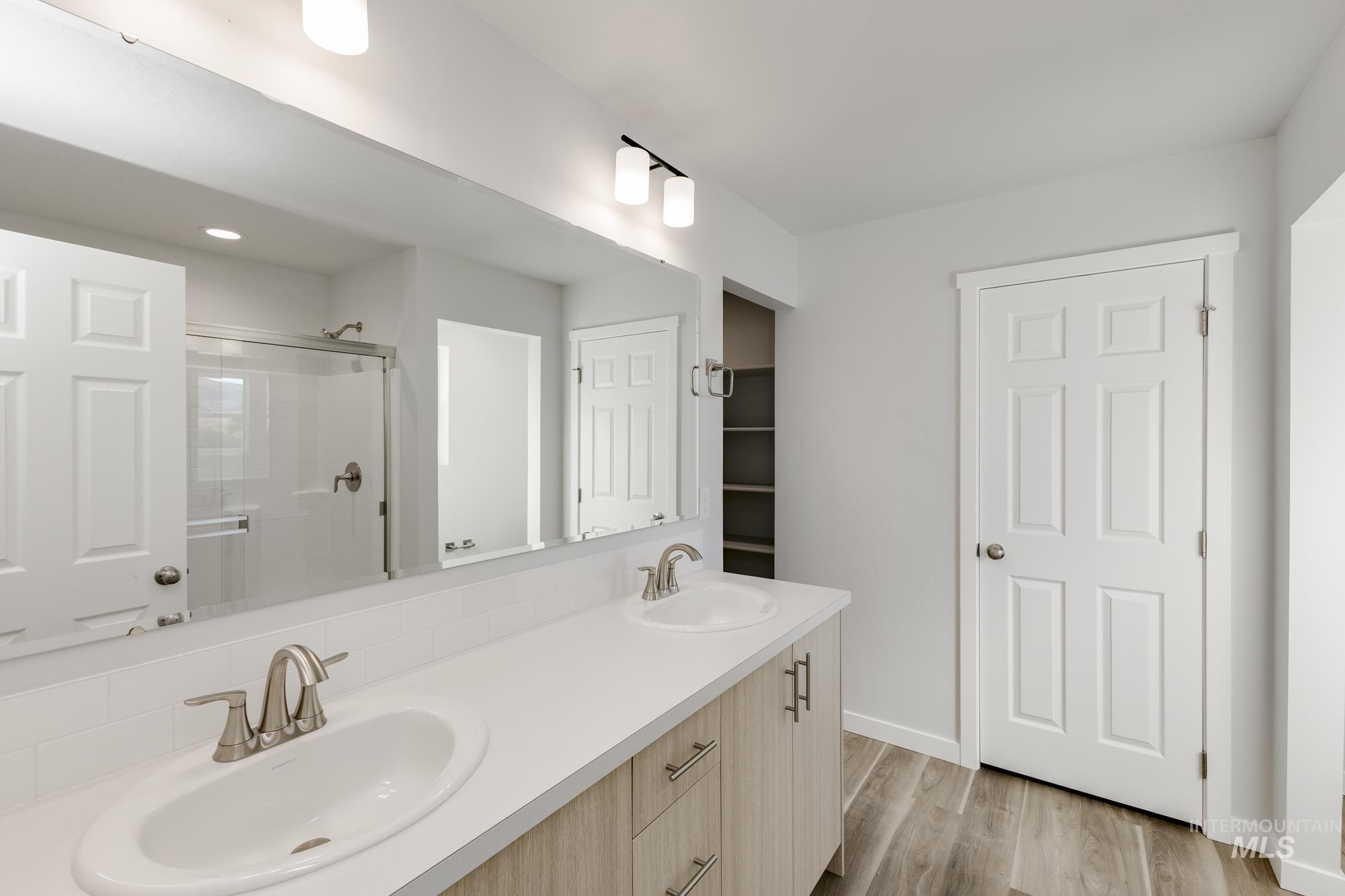 Full bath featuring double vanity, light wood-style flooring, and a stall shower