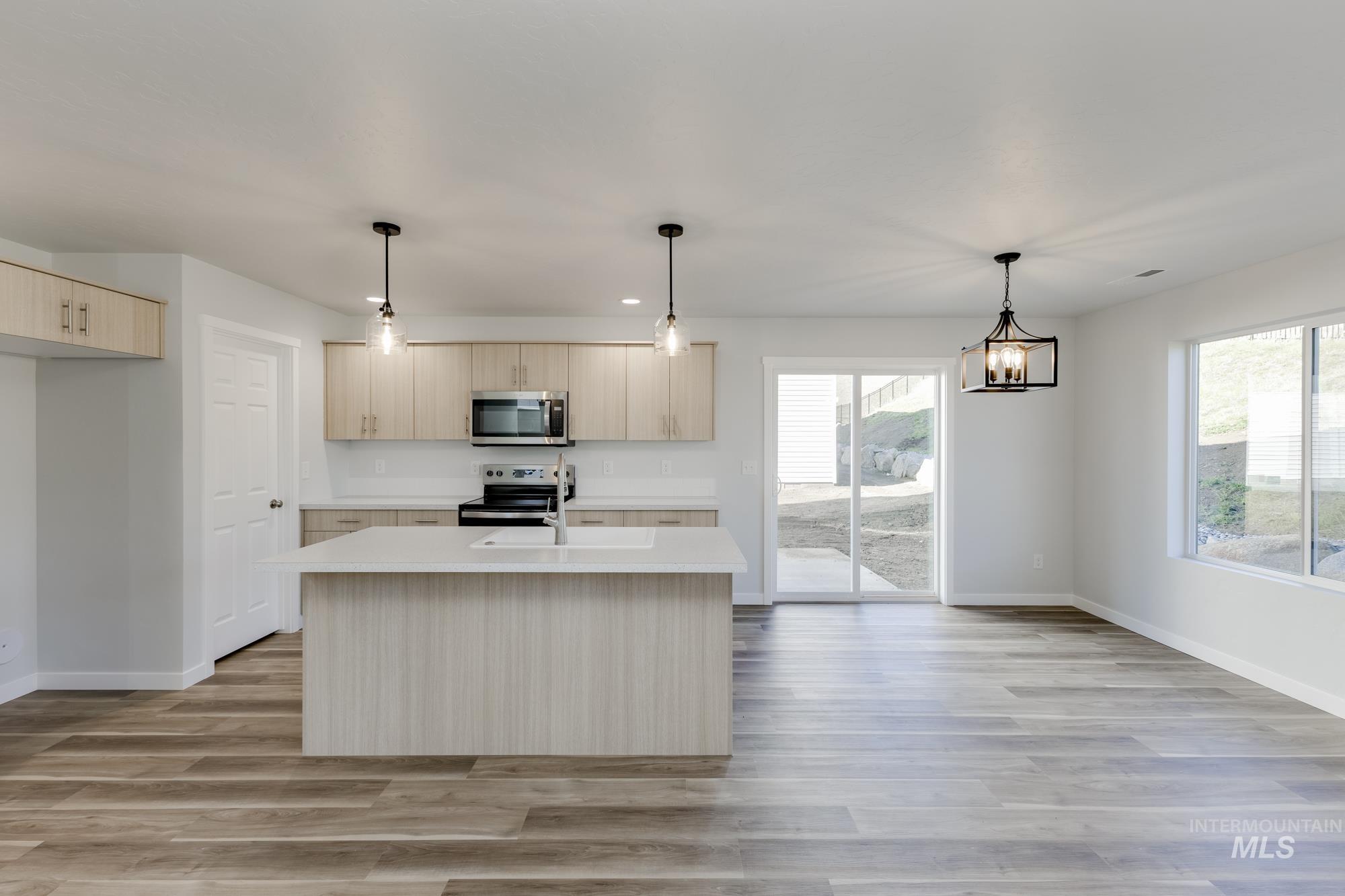 Kitchen featuring light countertops, hanging light fixtures, an island with sink, stainless steel appliances, and light wood-type flooring