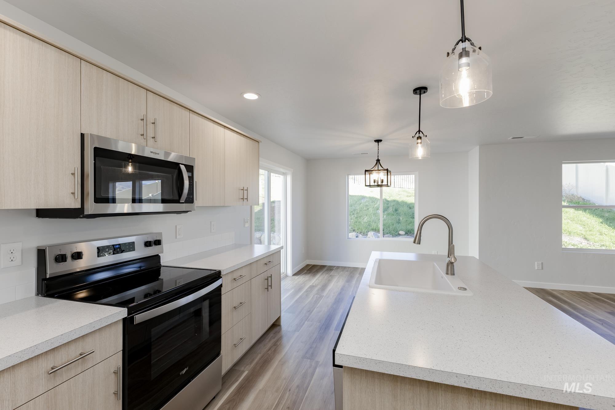 Kitchen with stainless steel appliances, light brown cabinets, light wood-style floors, hanging light fixtures, and recessed lighting