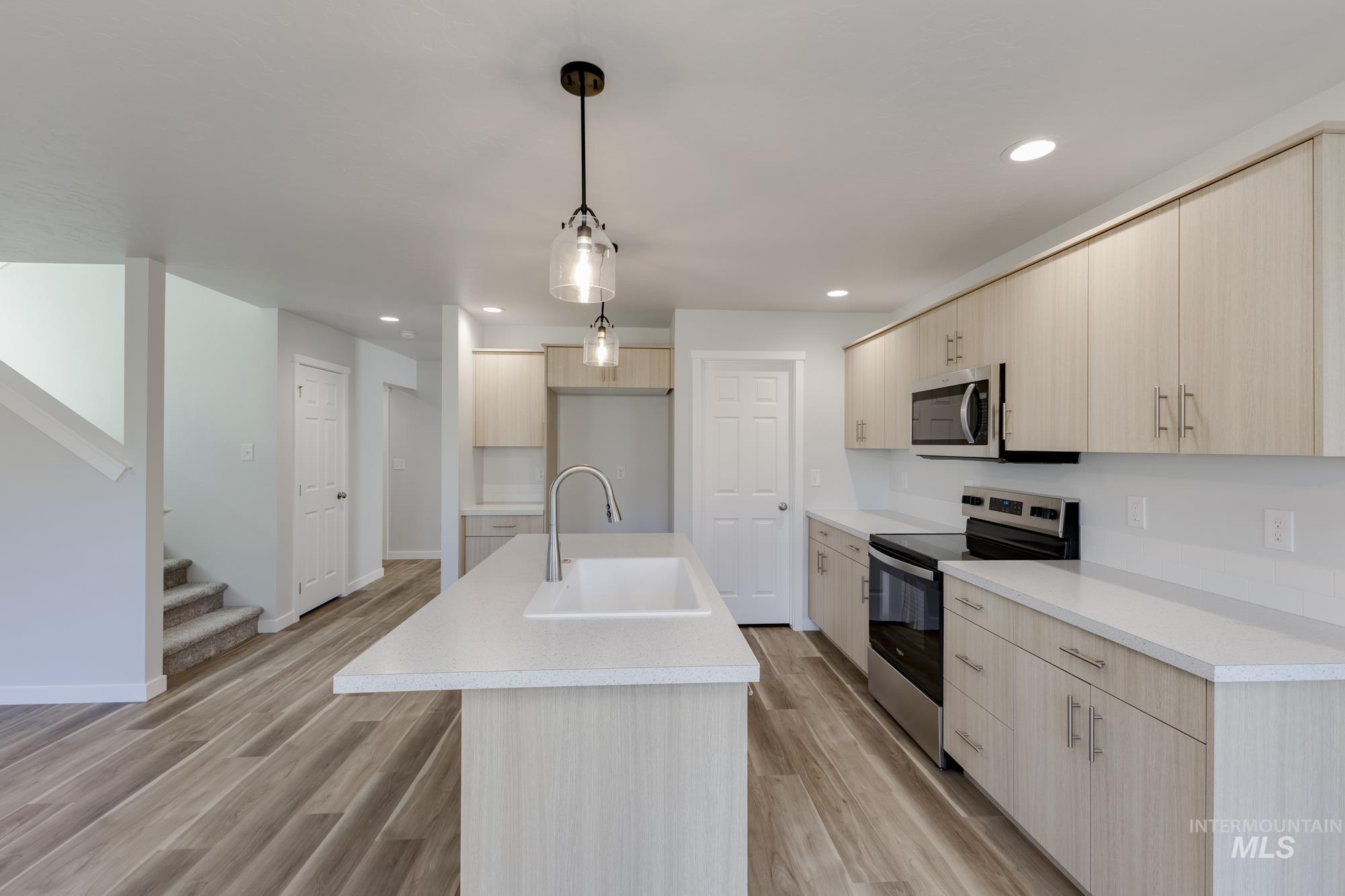 Kitchen featuring appliances with stainless steel finishes, light brown cabinetry, light countertops, a kitchen island with sink, and decorative light fixtures