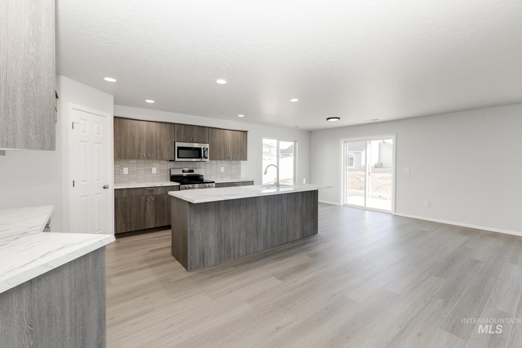Kitchen with modern cabinets, decorative backsplash, an island with sink, stainless steel appliances, and light wood-type flooring