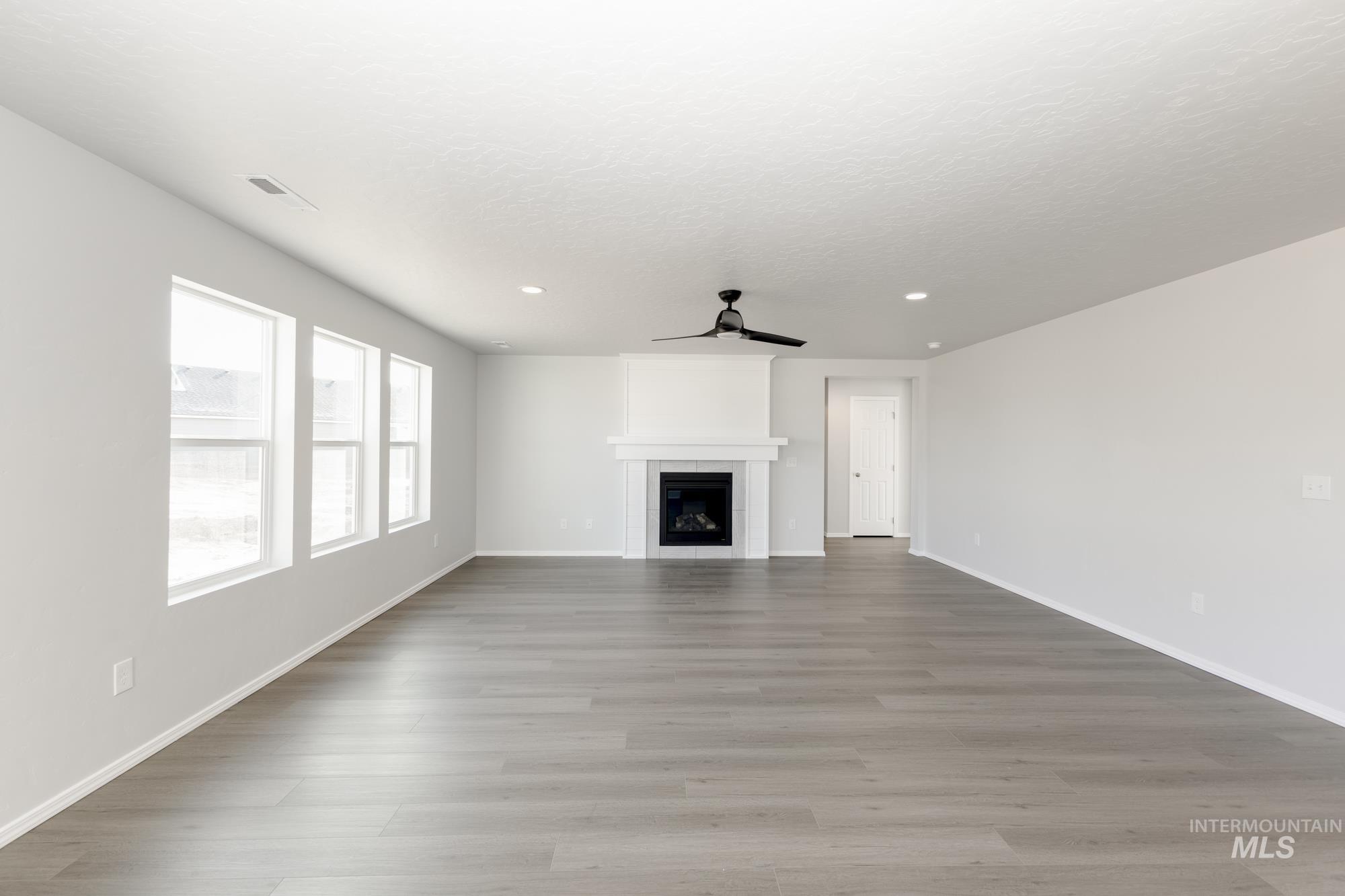 Unfurnished living room featuring light wood-type flooring, a ceiling fan, a tiled fireplace, and recessed lighting